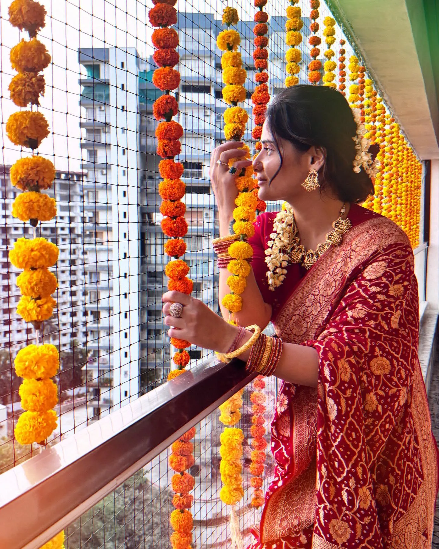 Arti Singh holding orange marigold decorations on a balcony