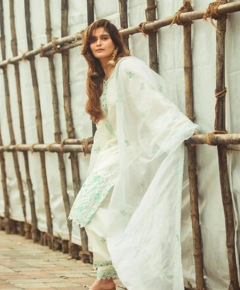 Arti Singh in a white floral dress sitting on wooden walkway