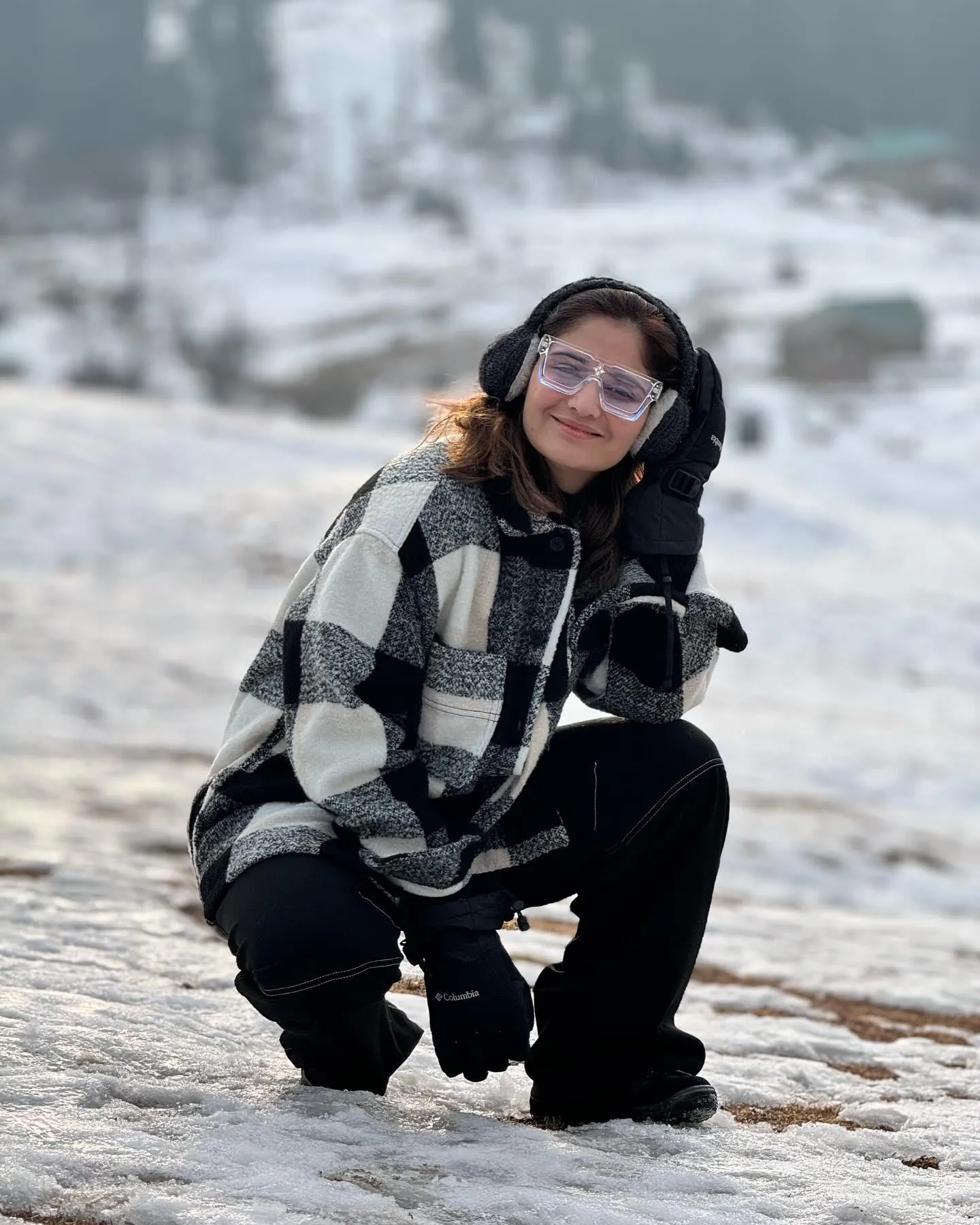 Arti Singh kneels in the snow wearing a cozy winter jacket
