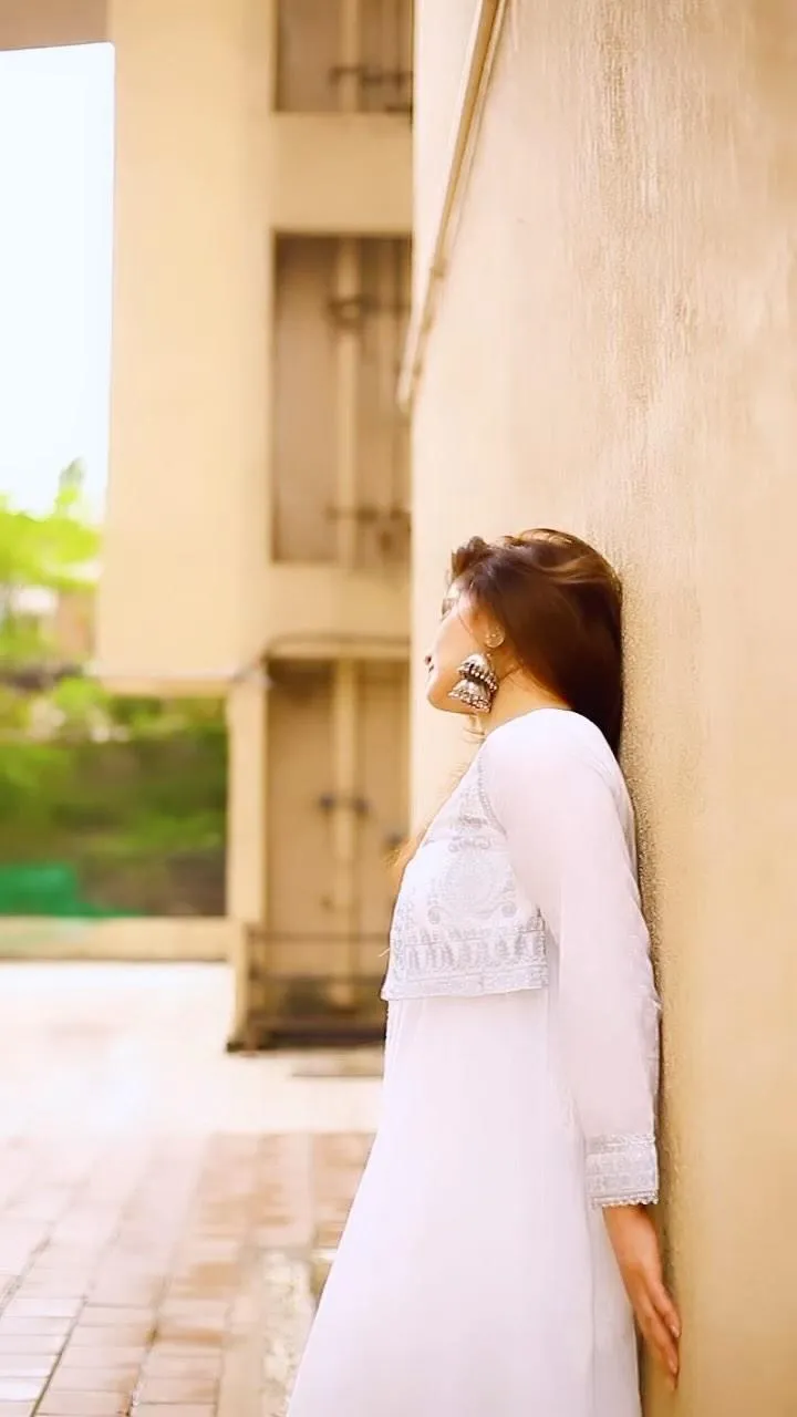 Arti Singh leans back against a wall in a simple white suit