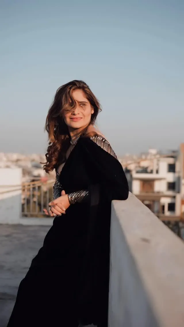 Arti Singh leans on the railing in a black modern outfit