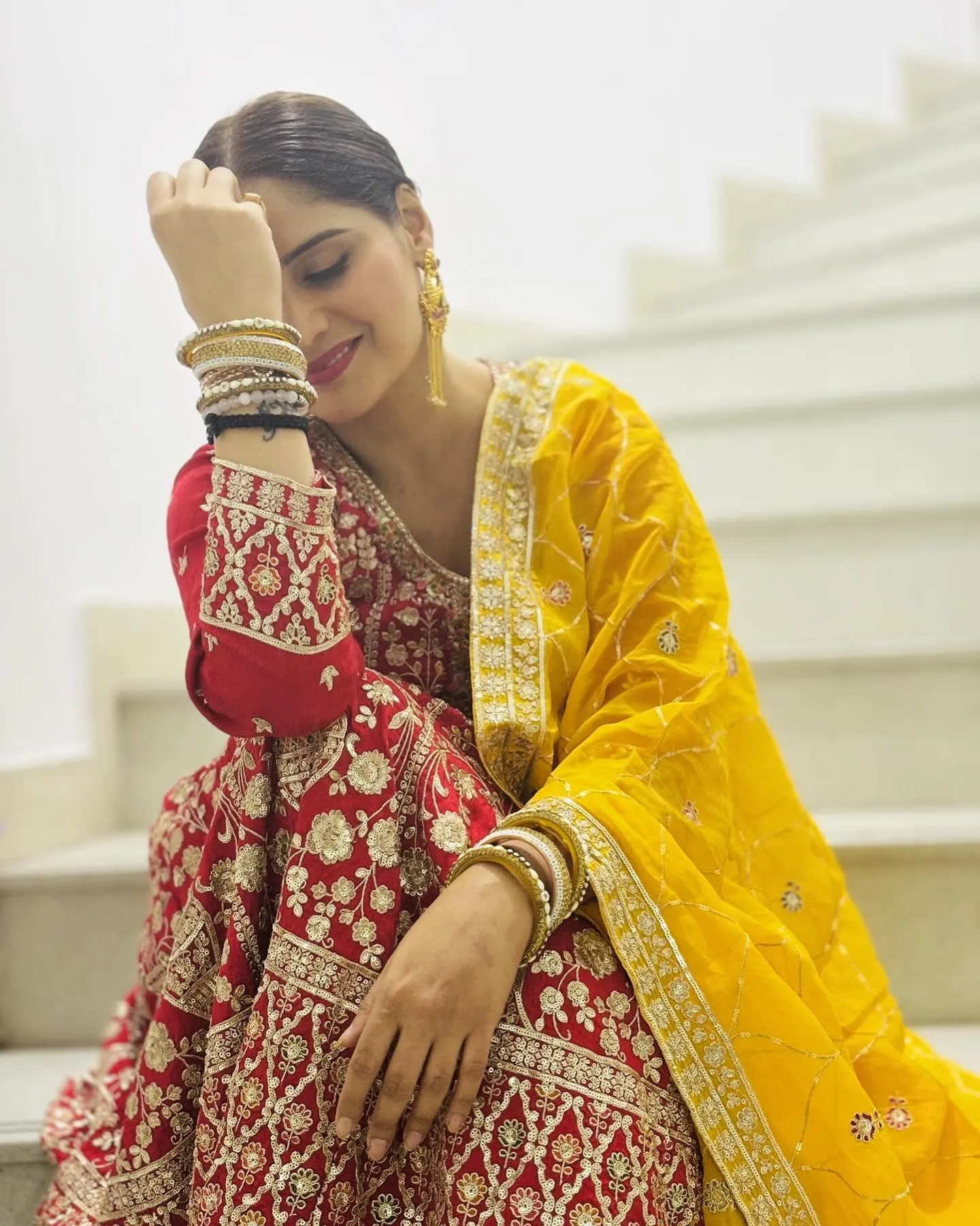 Arti Singh sits  in a red outfit with a yellow dupatta image