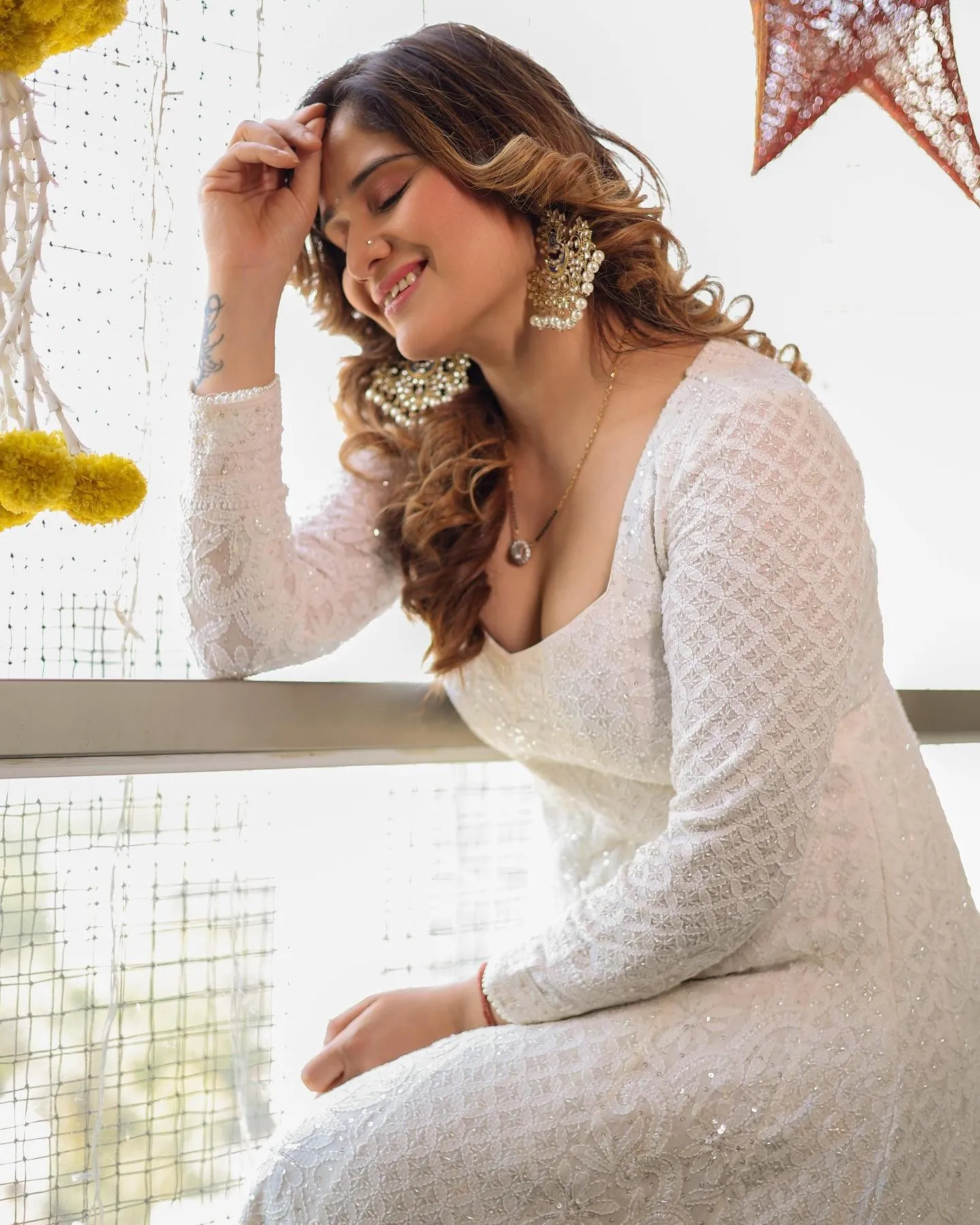 Arti Singh sits elegantly in a white dress with soft makeup