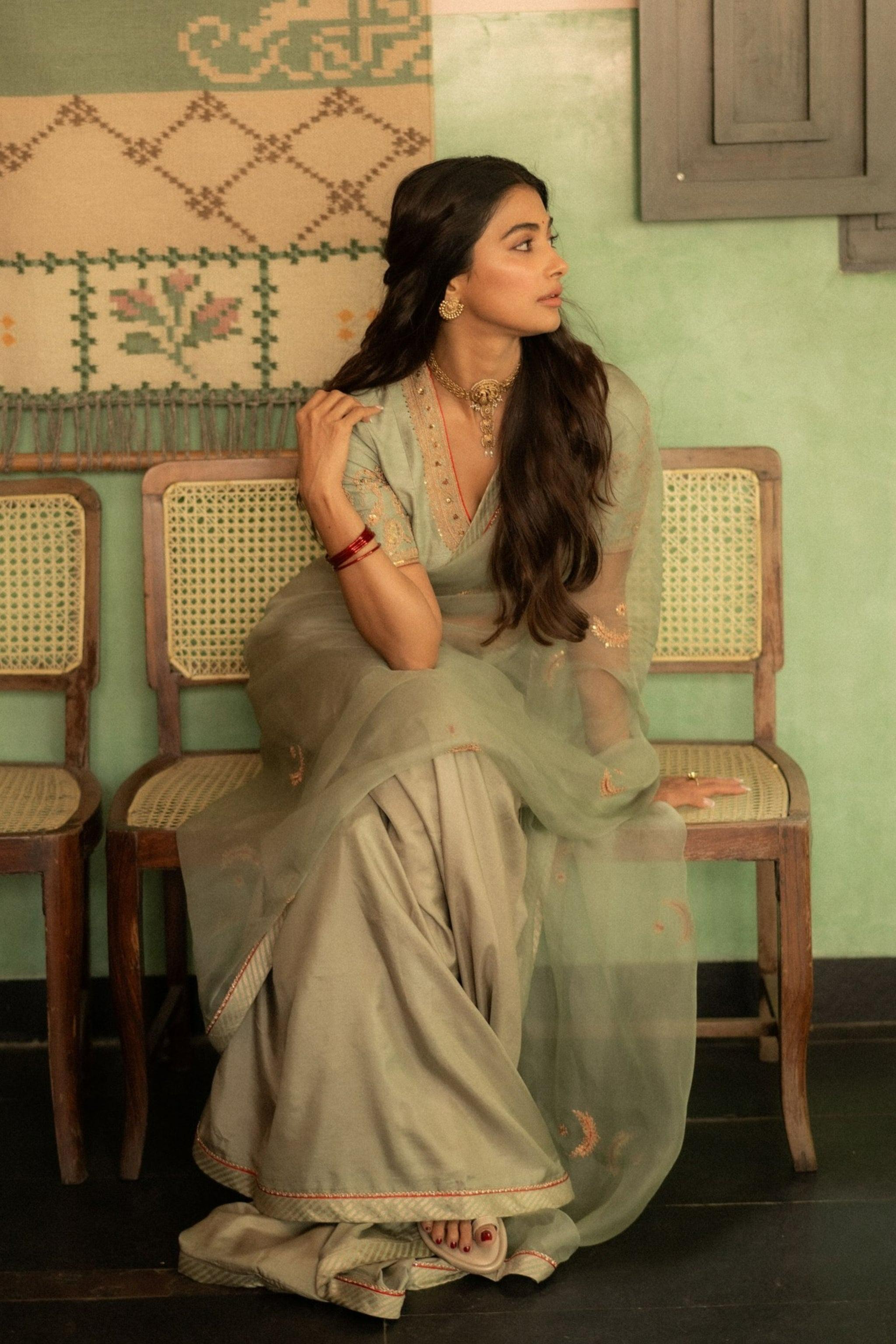 Graceful Pooja Hegde in Green Saree on Antique Wooden Chair