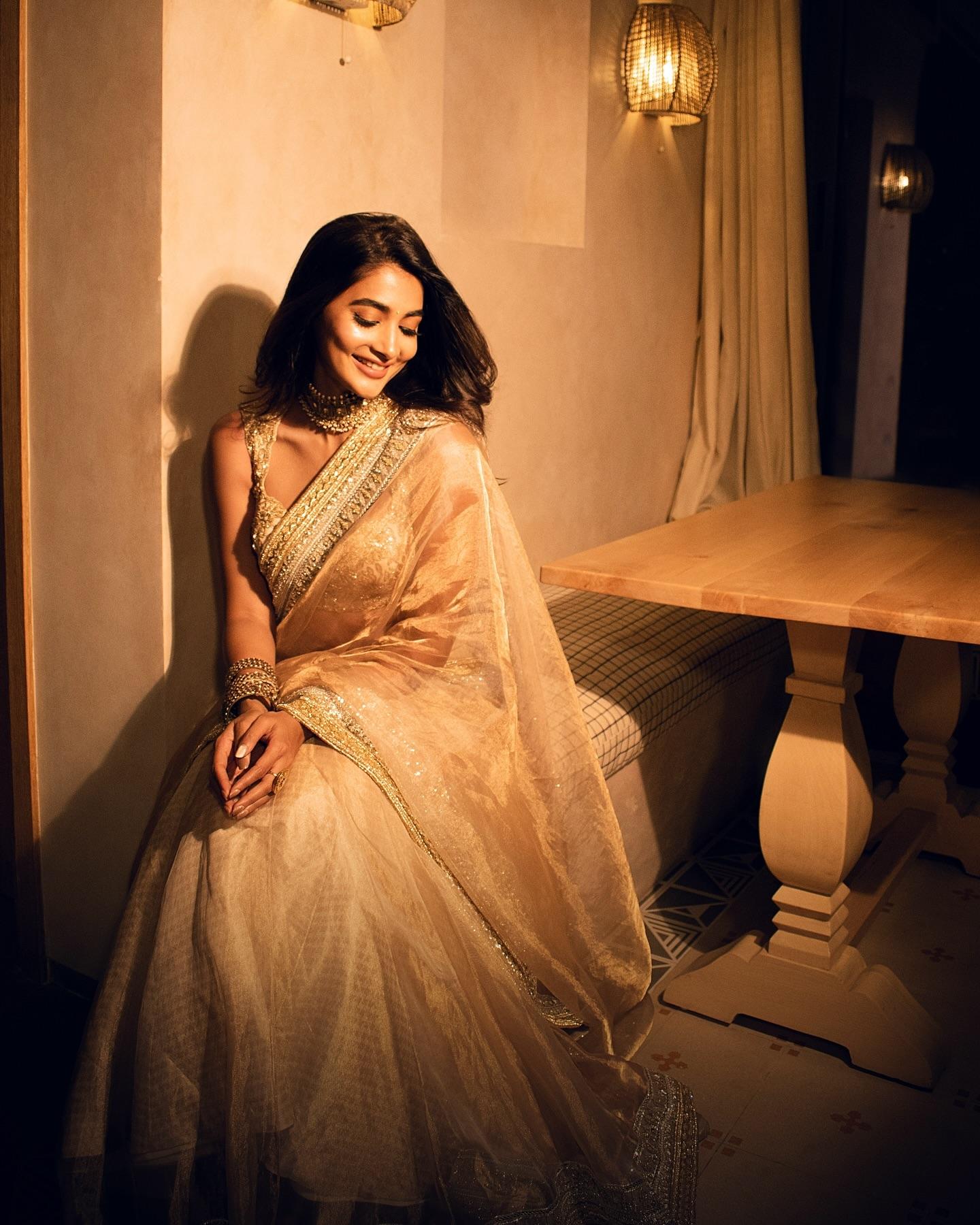 Pooja Hegde in Gold Saree Smiling Near Wooden Table Image