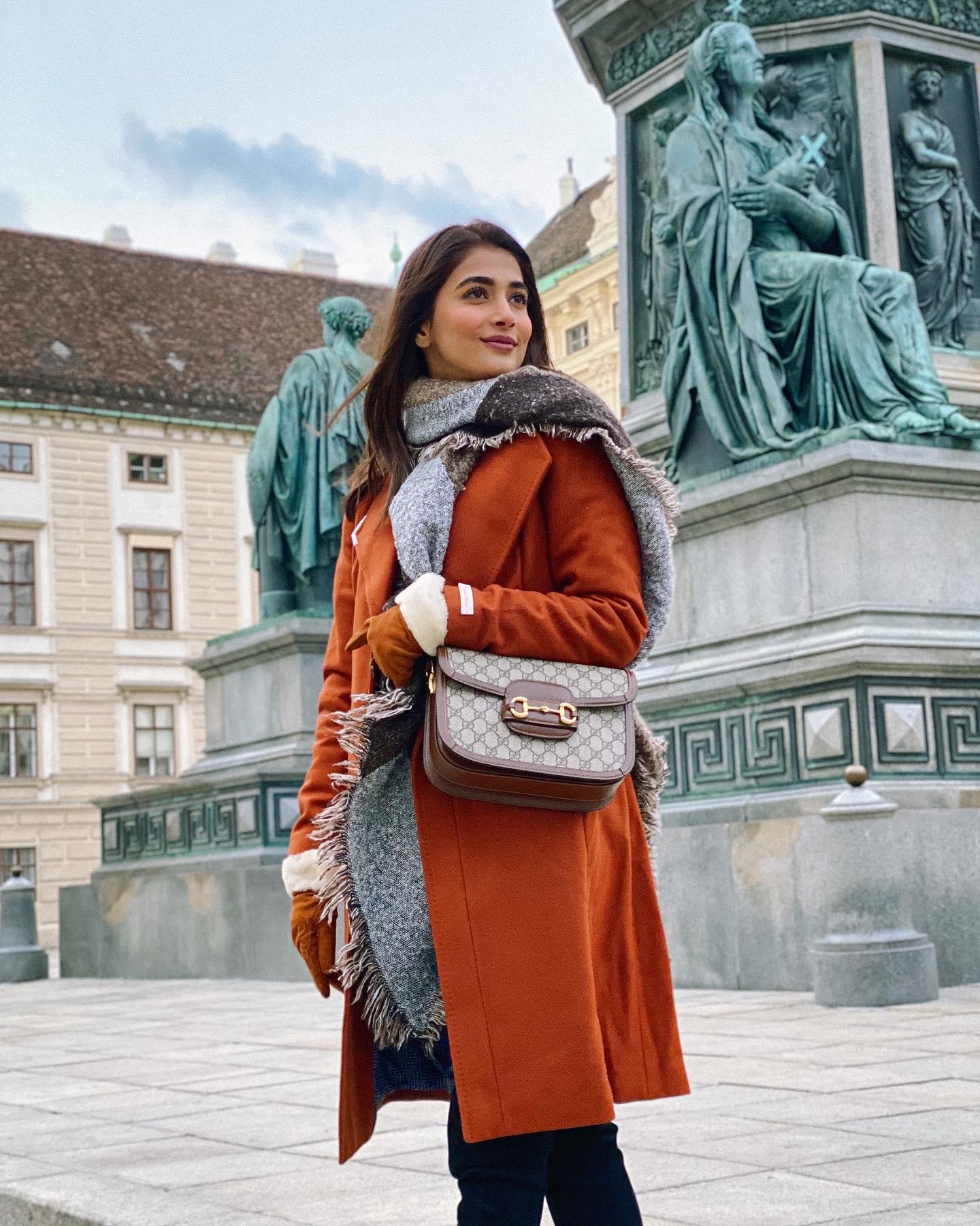 Pooja Hegde in Rust Coat with City Sculpture Backdrop