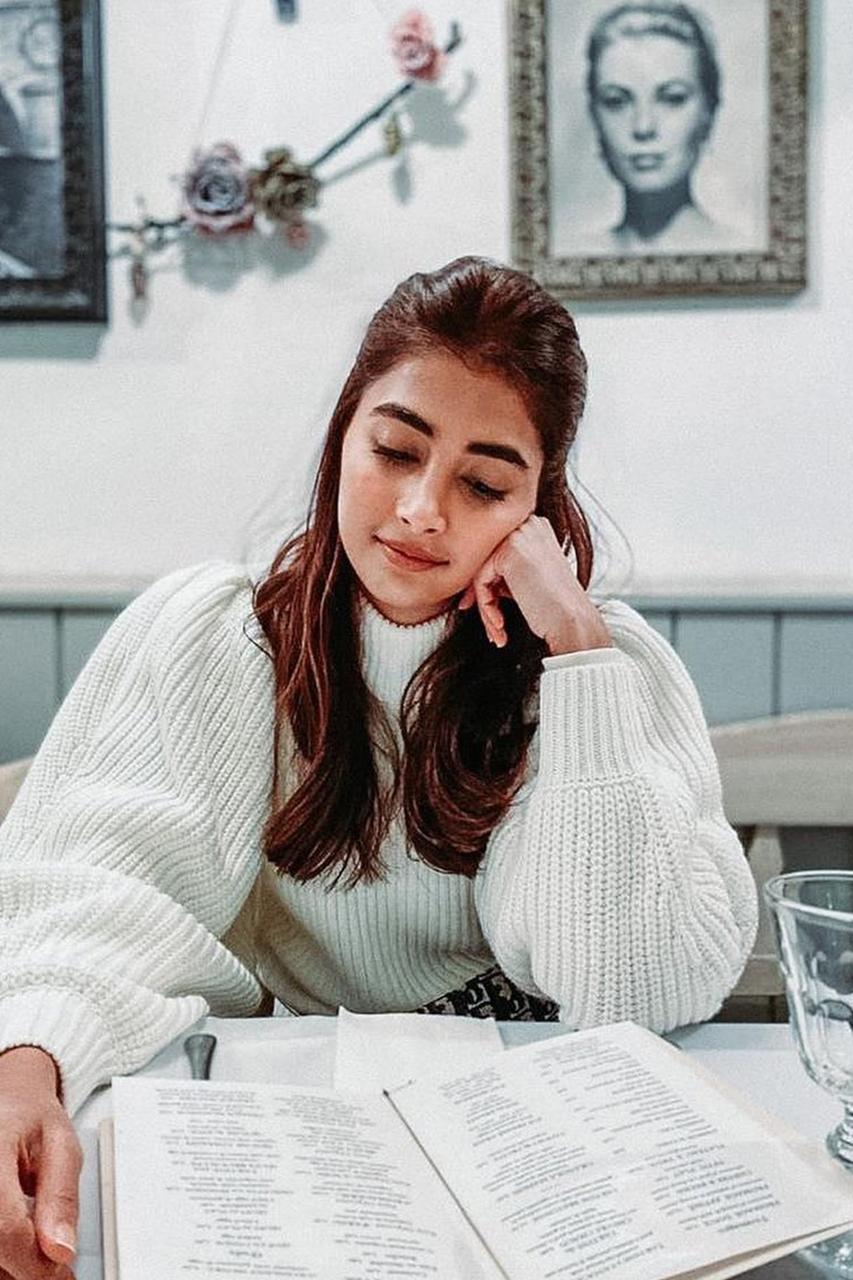 Pooja Hegde in White Sweater Reading At a Cafe Table