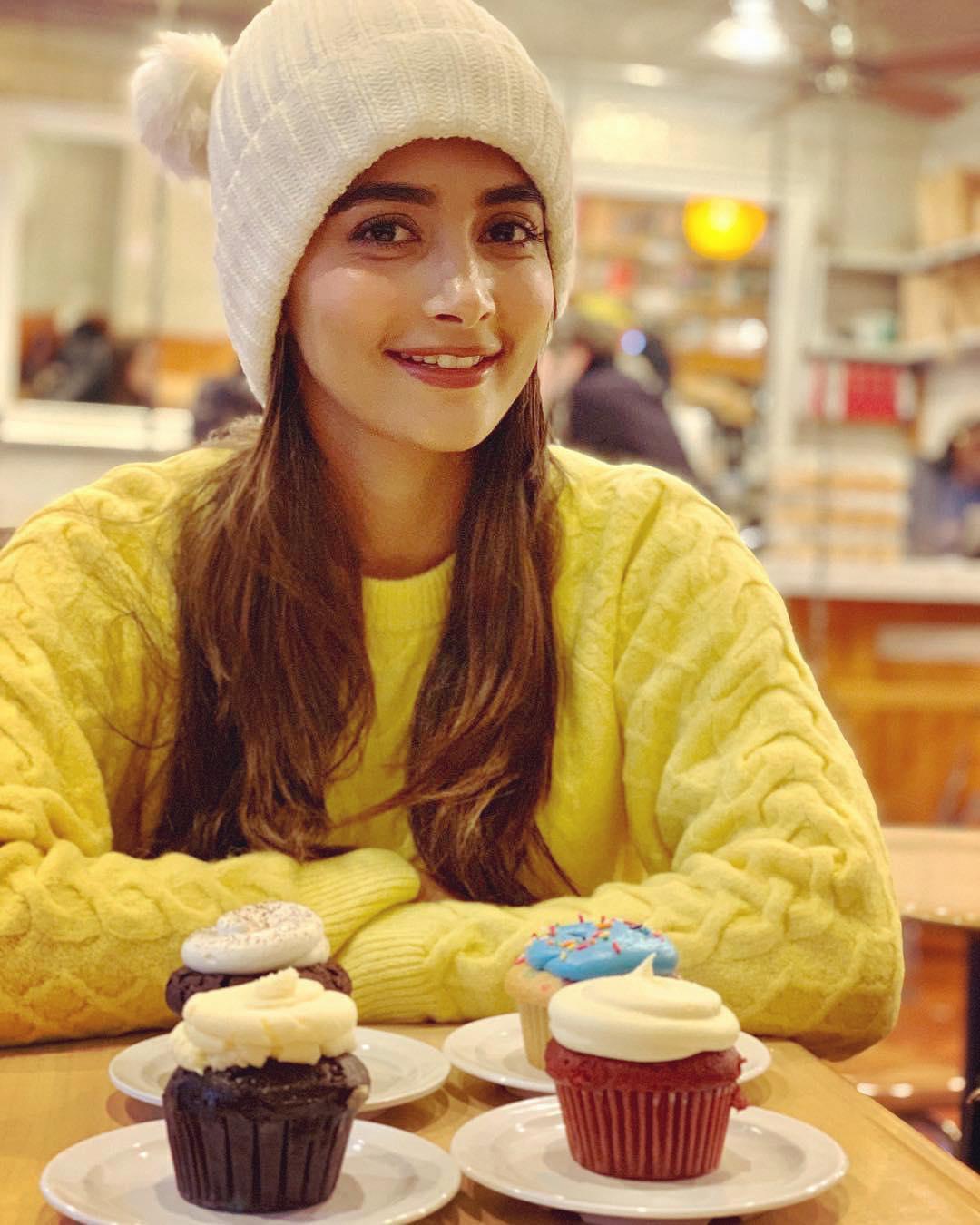 Pooja Hegde in Yellow Sweater Smiling with Cupcakes on Table
