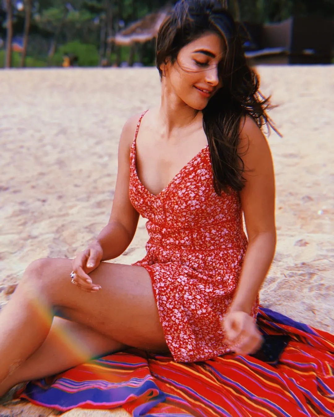 Joyful Pooja Hegde Sitting on Beach in Red Dress Image