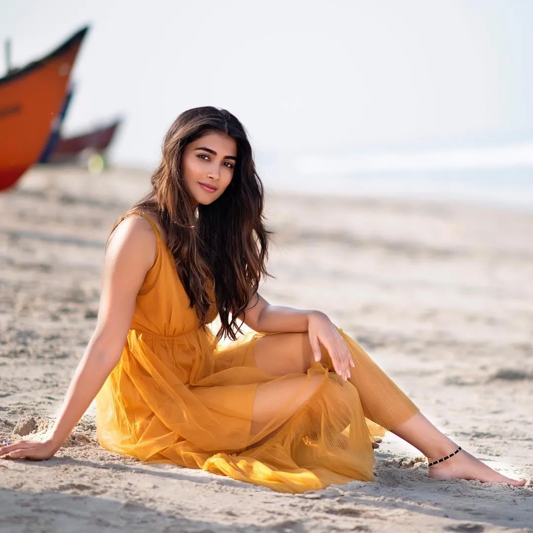 Pooja Hegde in Orange Dress Sitting on Beach Sand Wallpaper