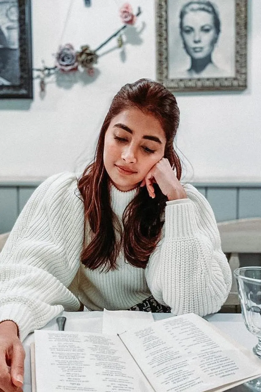 Pooja Hegde in White Sweater Reading At a Cafe Table