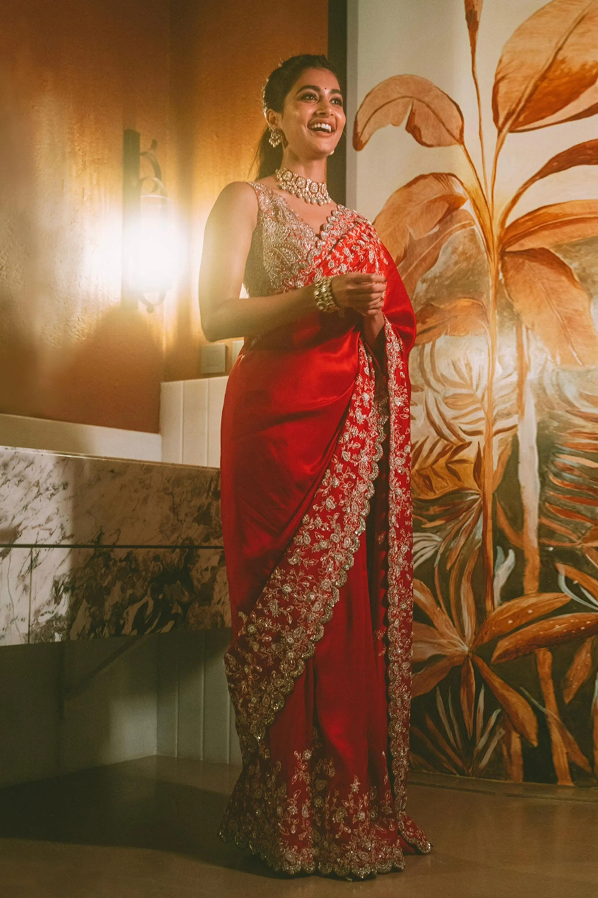 Pooja Hegde Poses in Red Saree Near Floral Mural Indoors