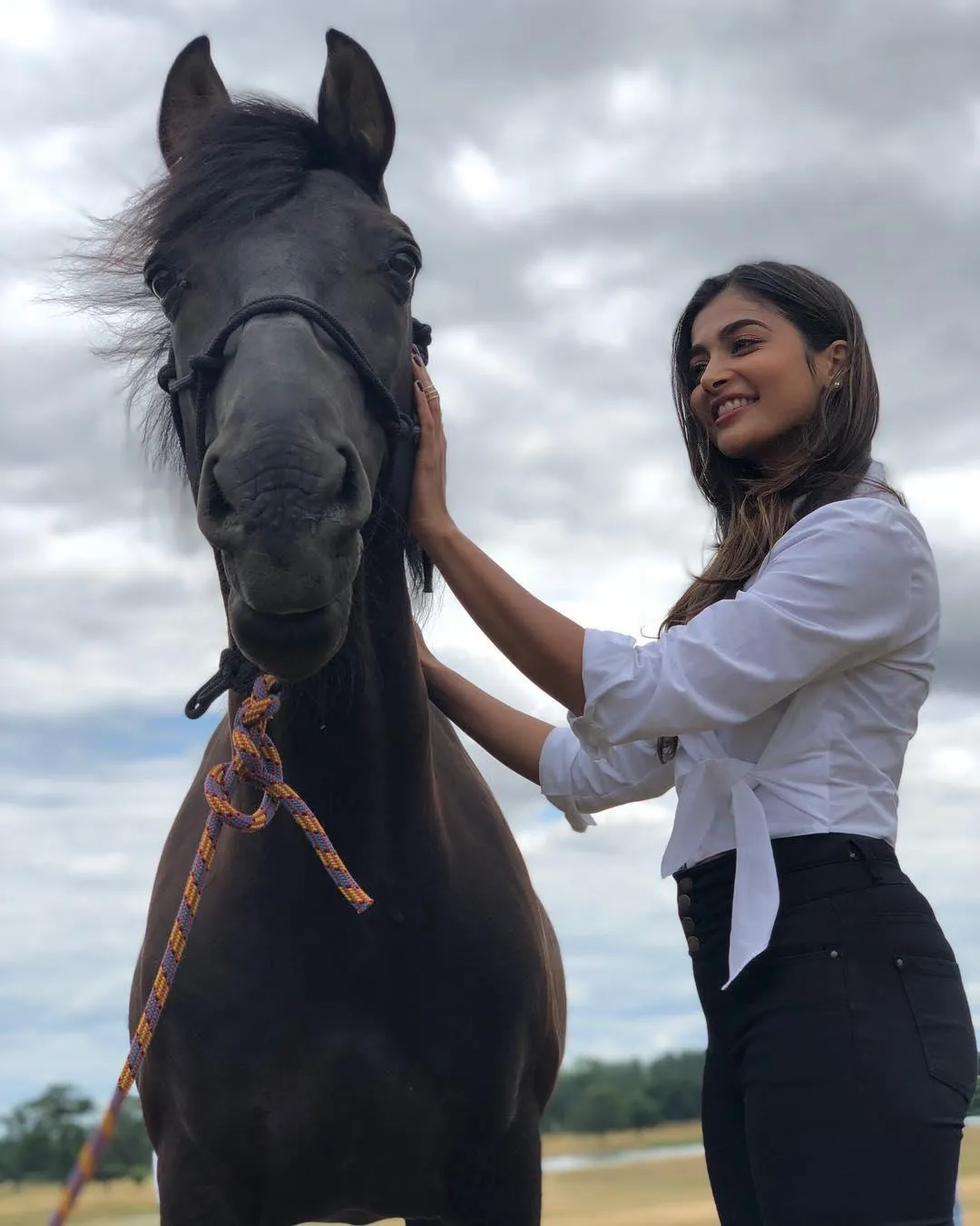 Pooja Hegde Smiling Beside a Black Horse in the Fields