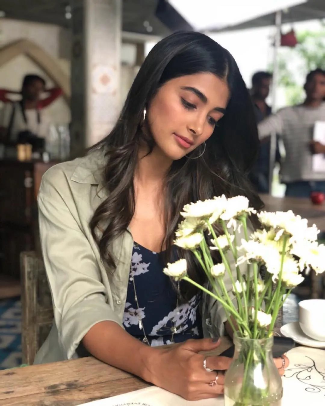 Pooja Hegde Writing While Sitting Near a Table with Flowers