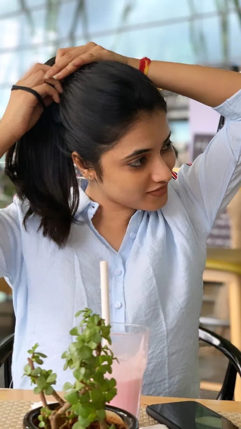 Priyanka in a blue shirt fixing hair with a plant near