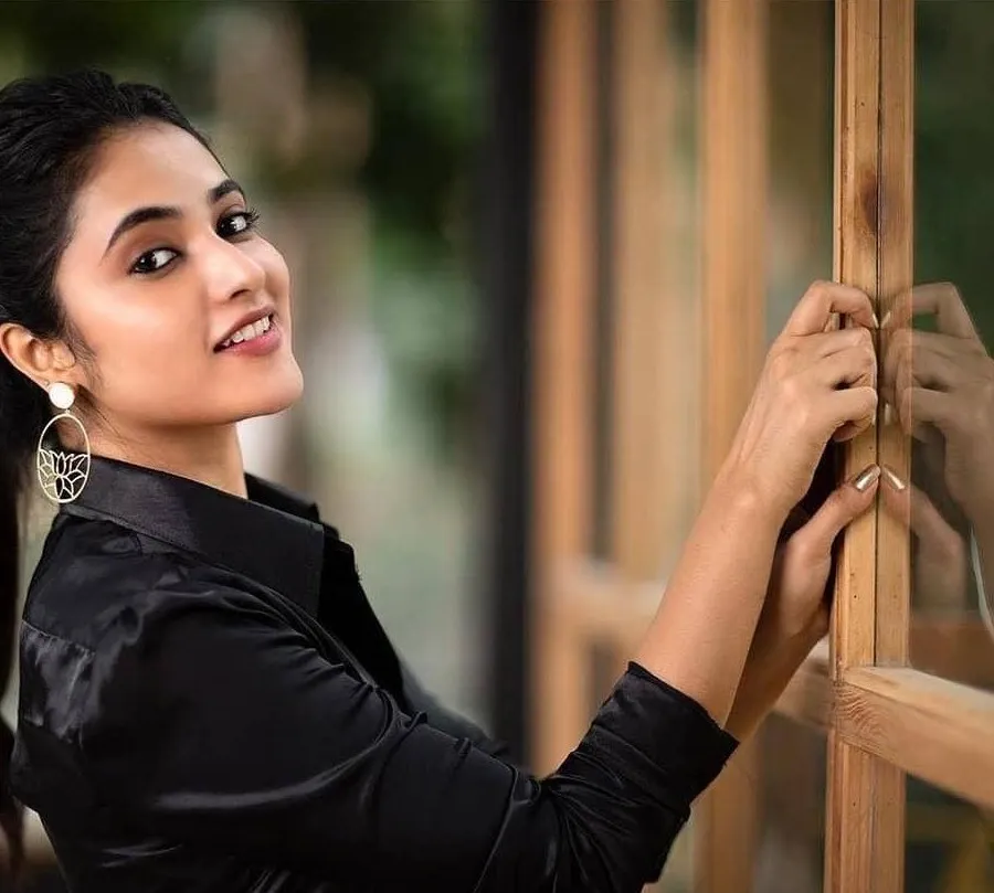 Priyanka in black dress smiling through wooden frame image