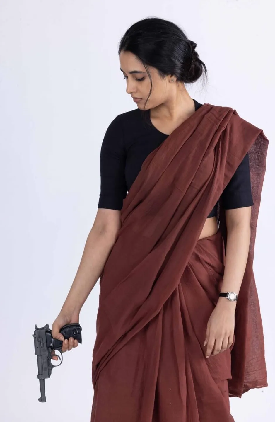 Priyanka in brown saree holding gun with a serious look