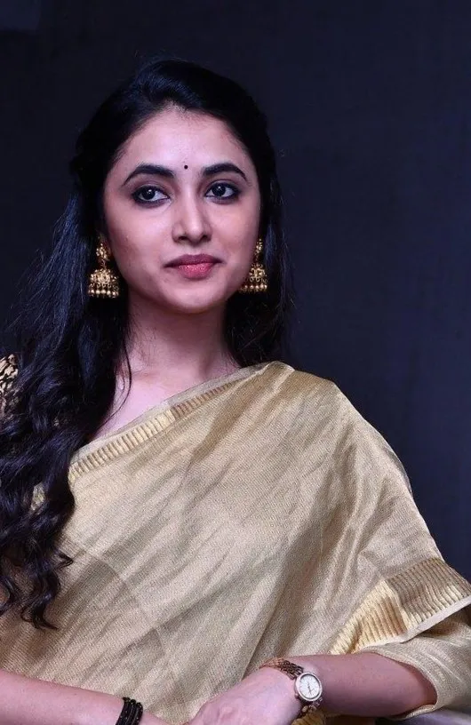 Priyanka in golden saree smiling against dark background