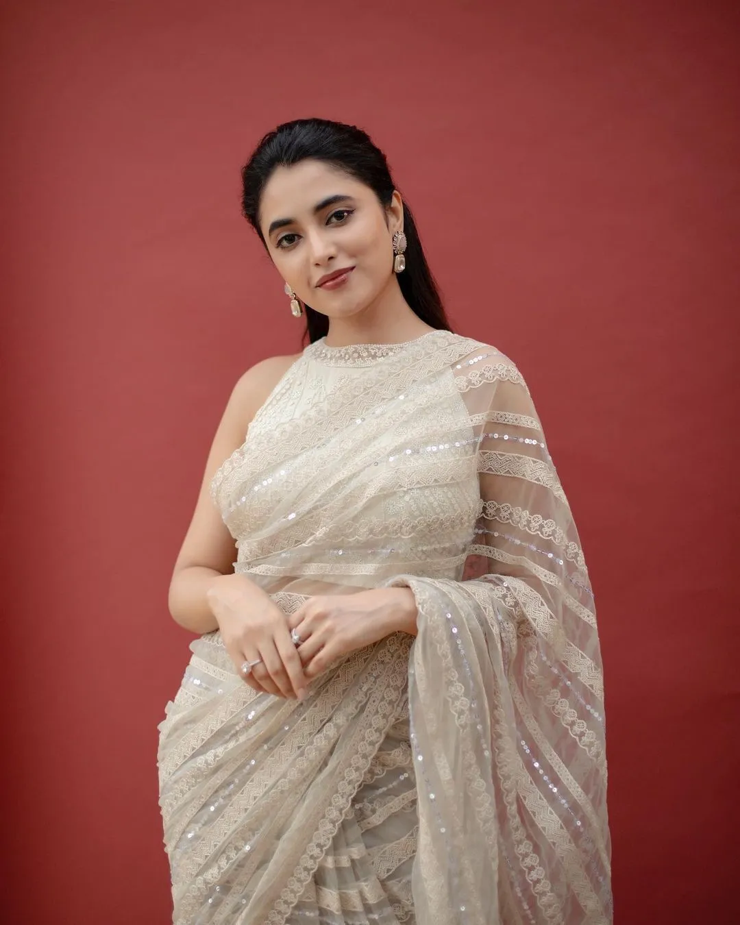 Priyanka in silver saree posing elegantly against red image