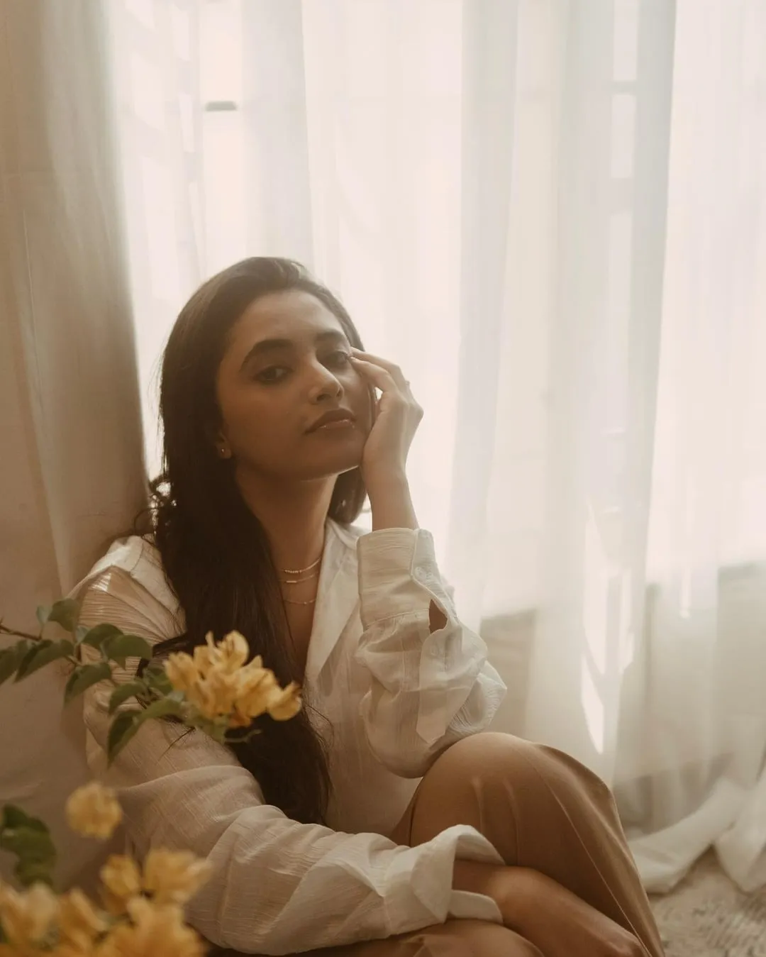 Priyanka in white dress sitting beside window with flowers