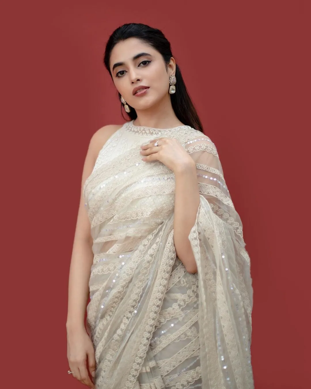 Priyanka in white saree standing against red background