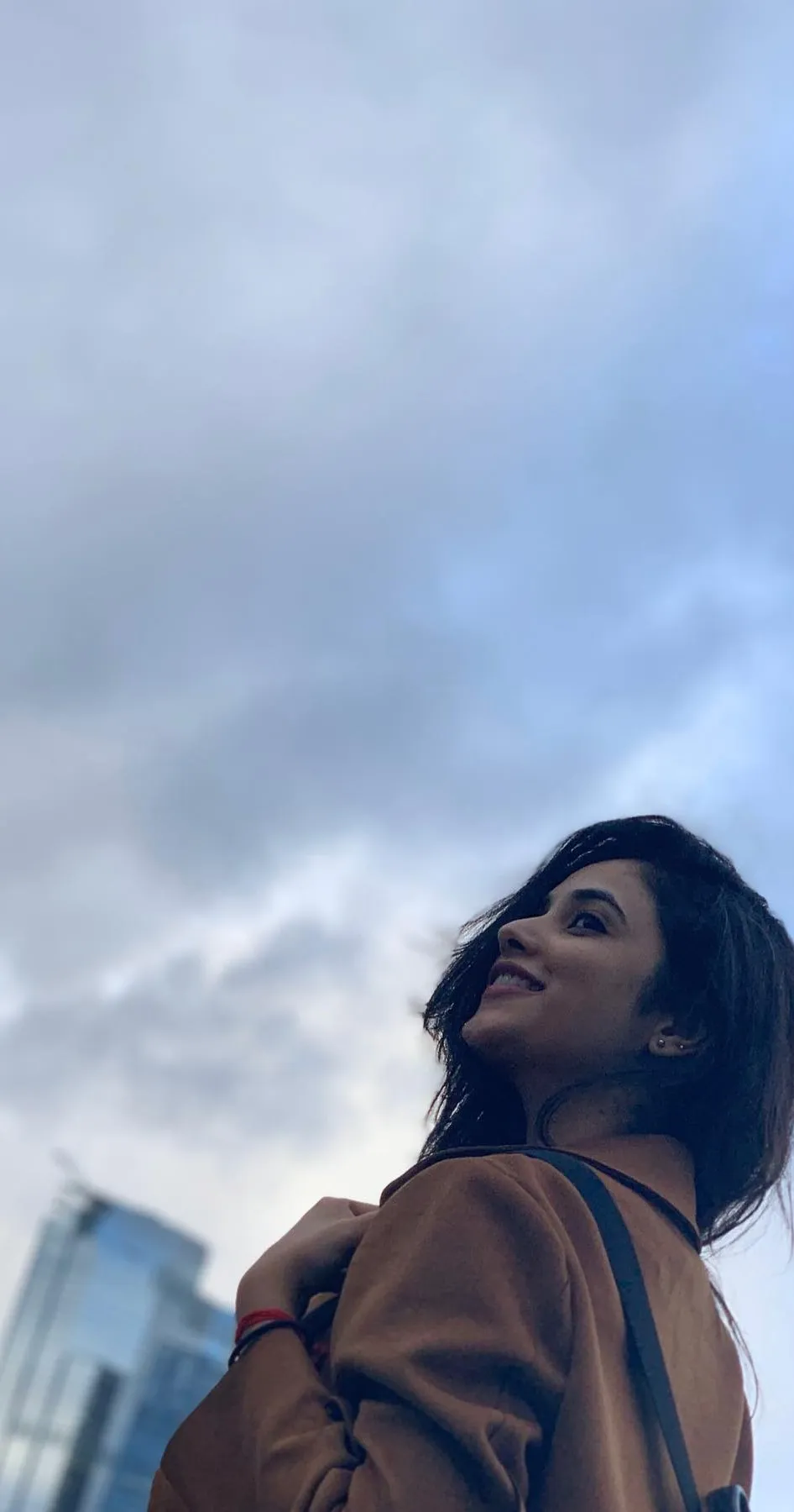 Priyanka looking up at cloudy sky in brown jacket Wallpaper