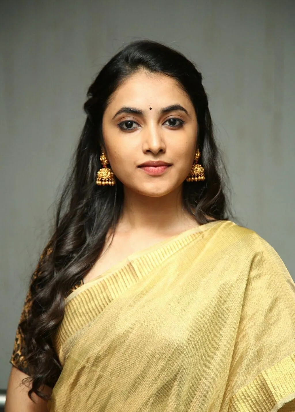 Priyanka Mohan in a Golden Saree Standing Against Gray Wall