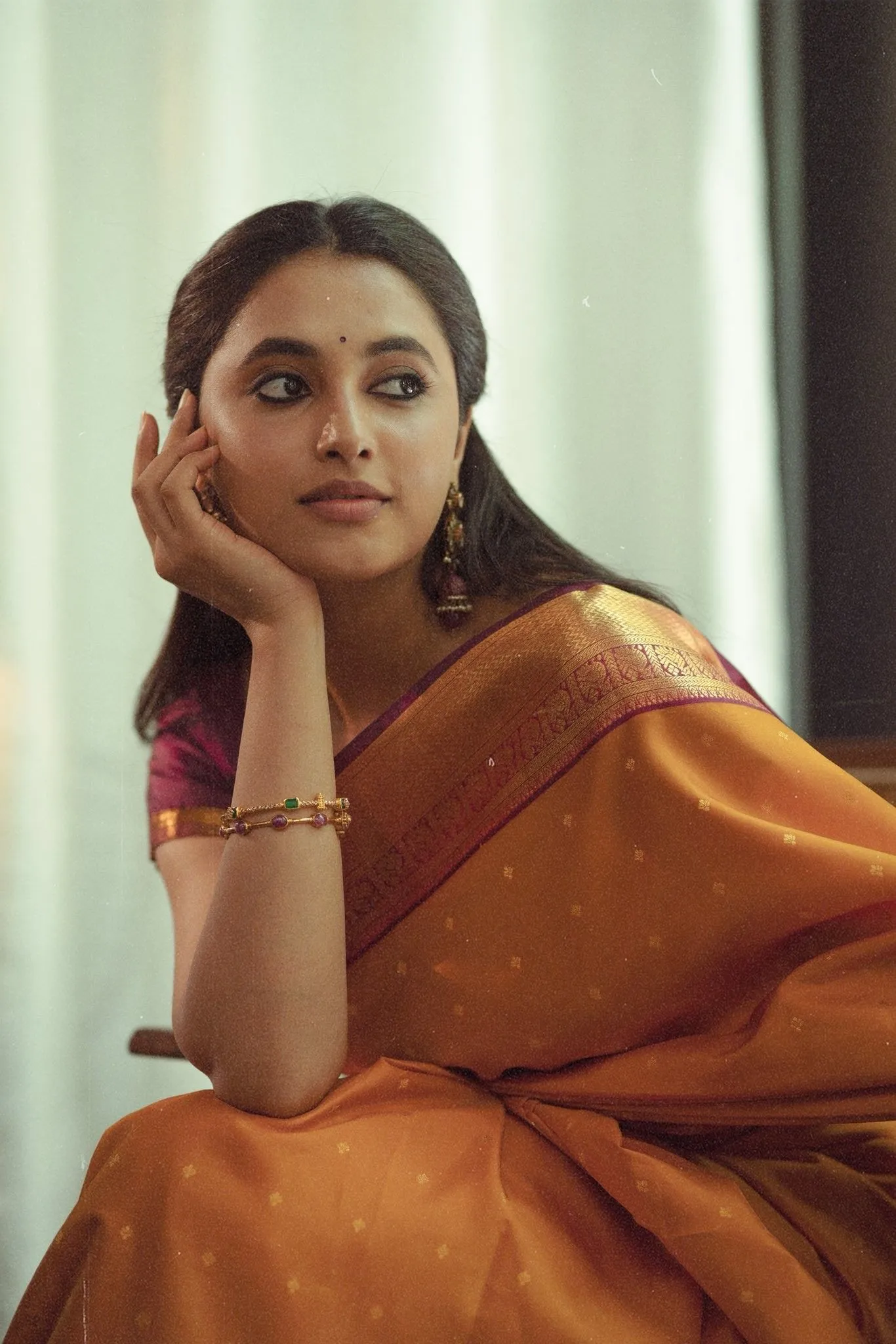 Priyanka Mohan in an Orange Saree Sitting on a Wooden Chair