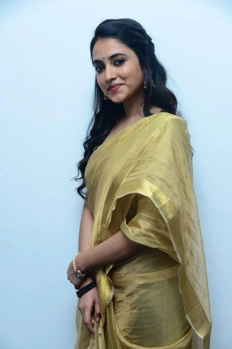 Priyanka standing in golden saree with side glance image