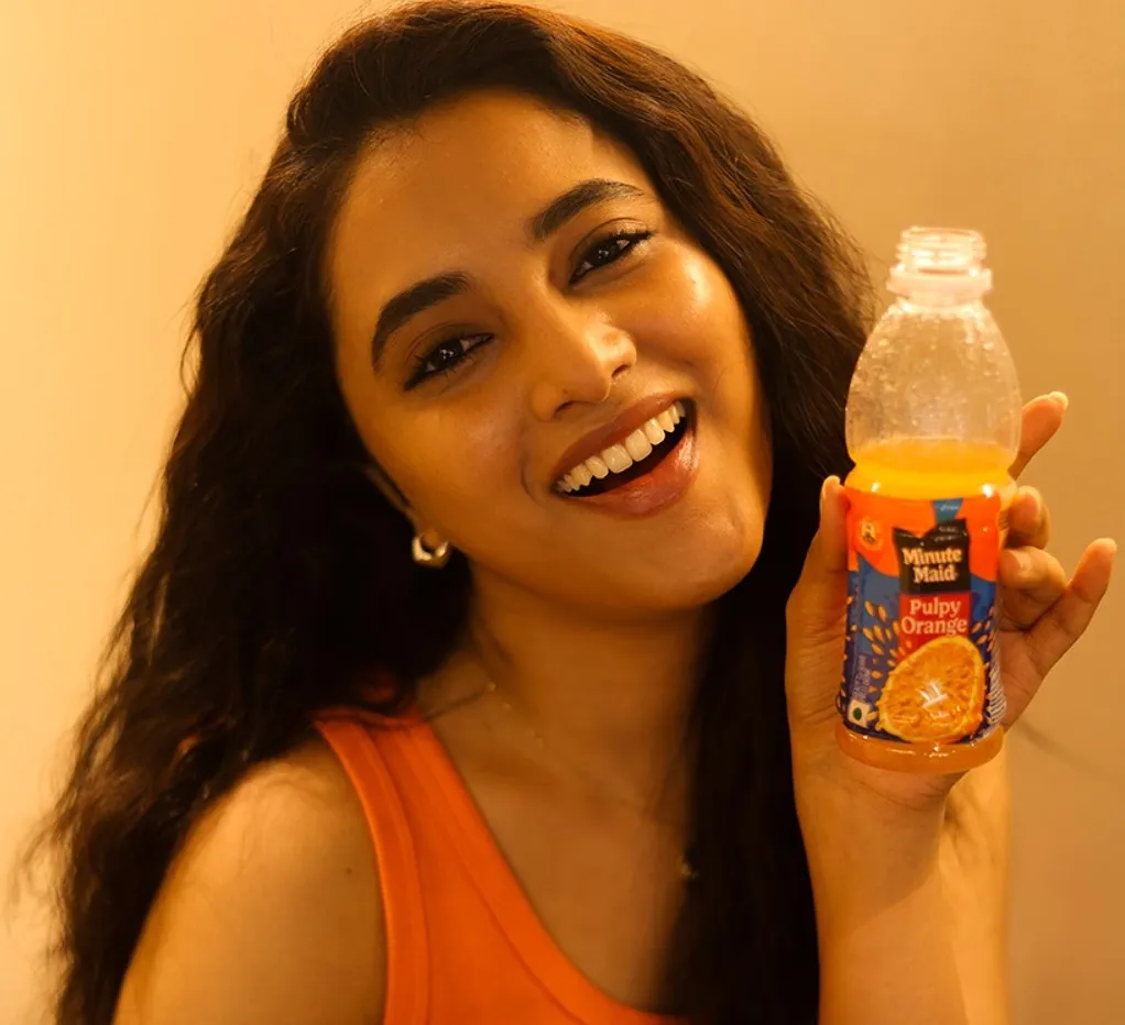 Smiling Priyanka holding drink in bright orange dress image