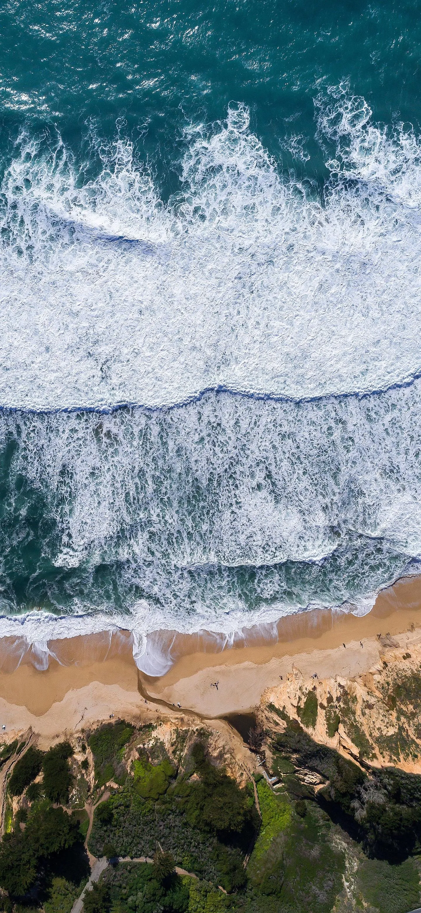 Aerial View of Ocean Waves Crashing Onto Rocky Sandy Shoreline