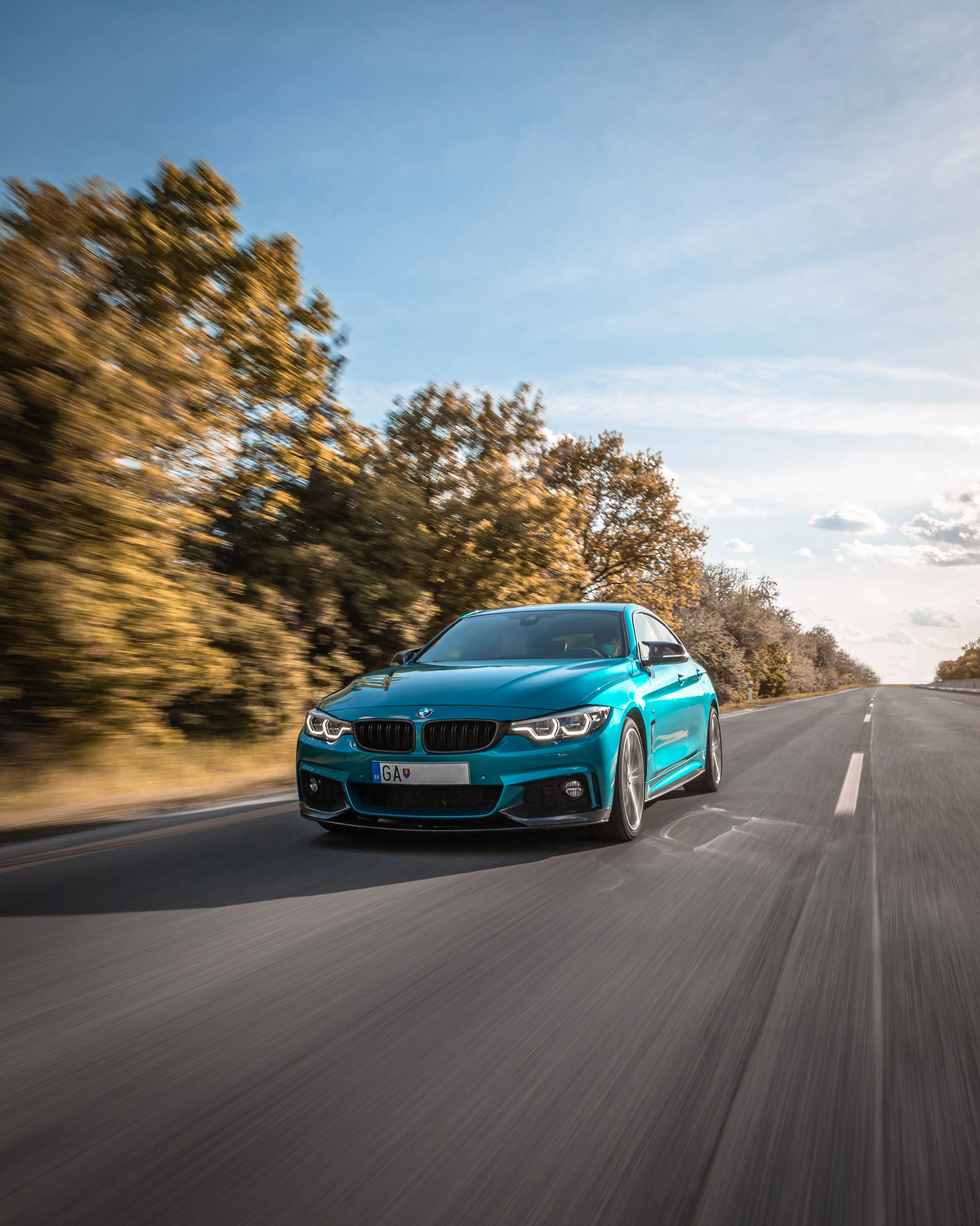 Blue Sports Car Driving Fast on Autumn Roadway Wallpaper
