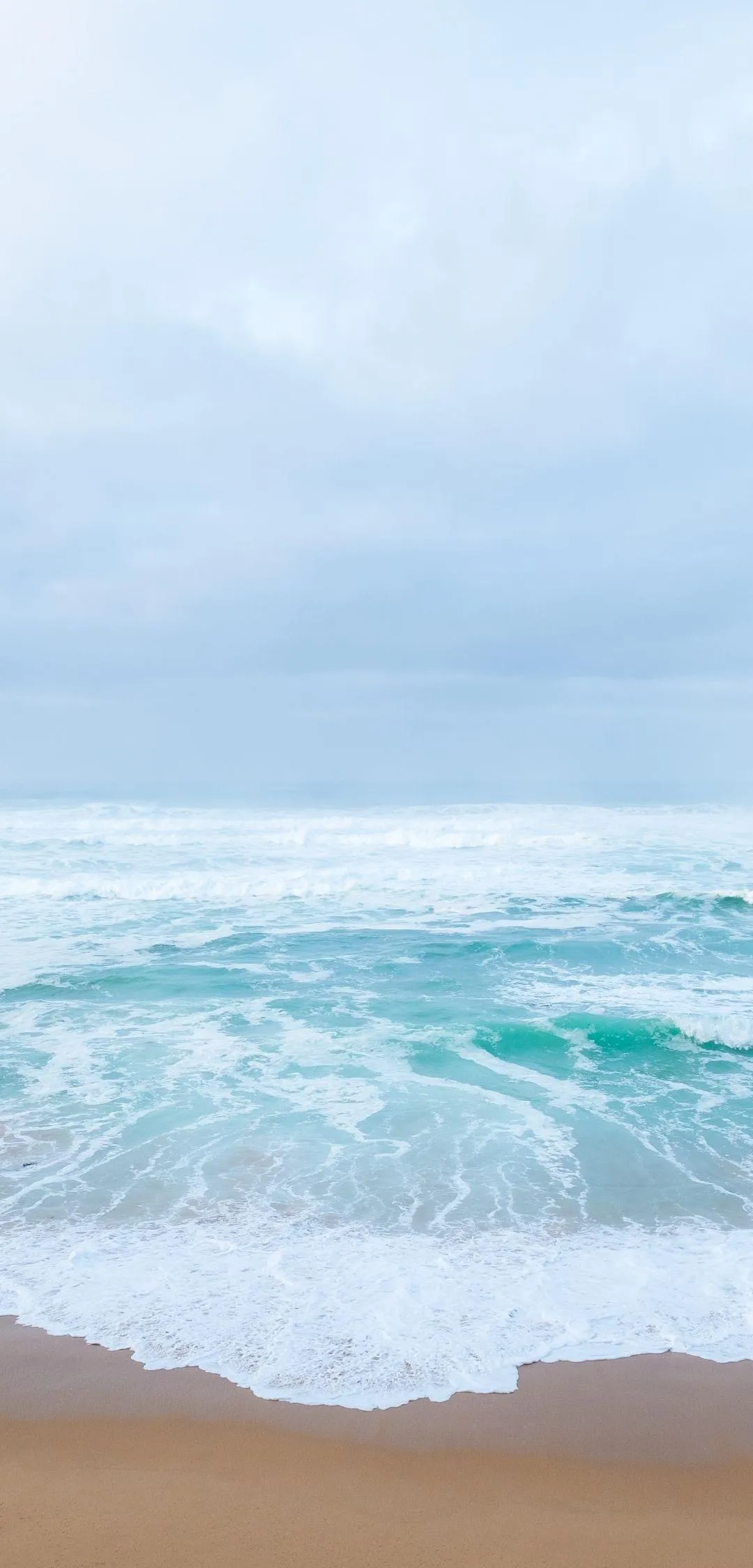 Calm Ocean Waves Crashing under Soft Blue Sky Wallpaper