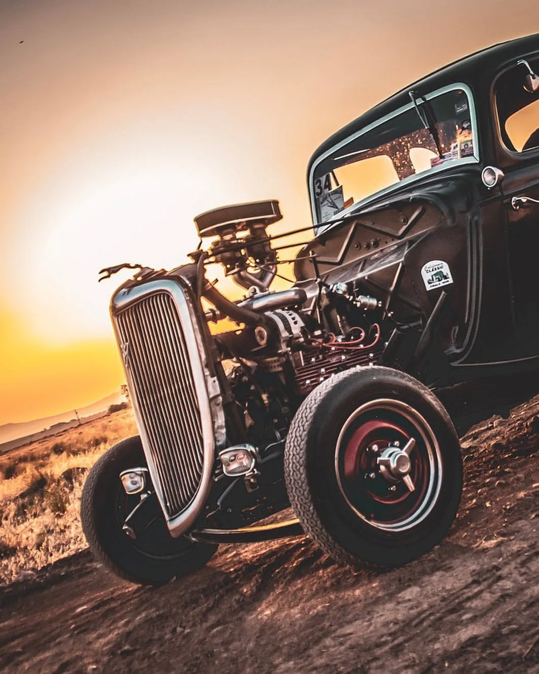 Classic Vintage Car at Sunset in Dusty Road Scene Wallpaper