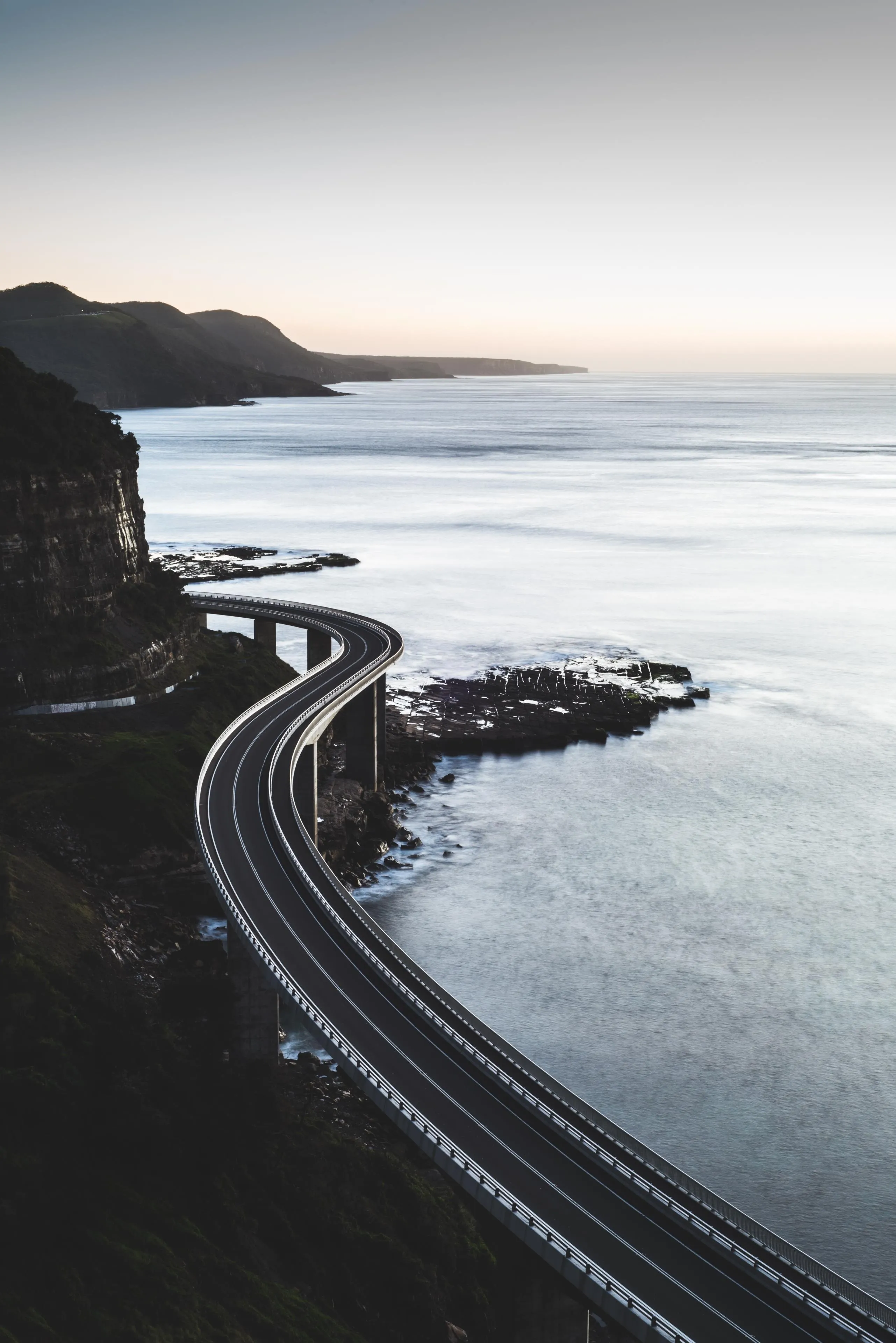 Curved Coastal Road Along Cliff with Calm Ocean Wallpaper