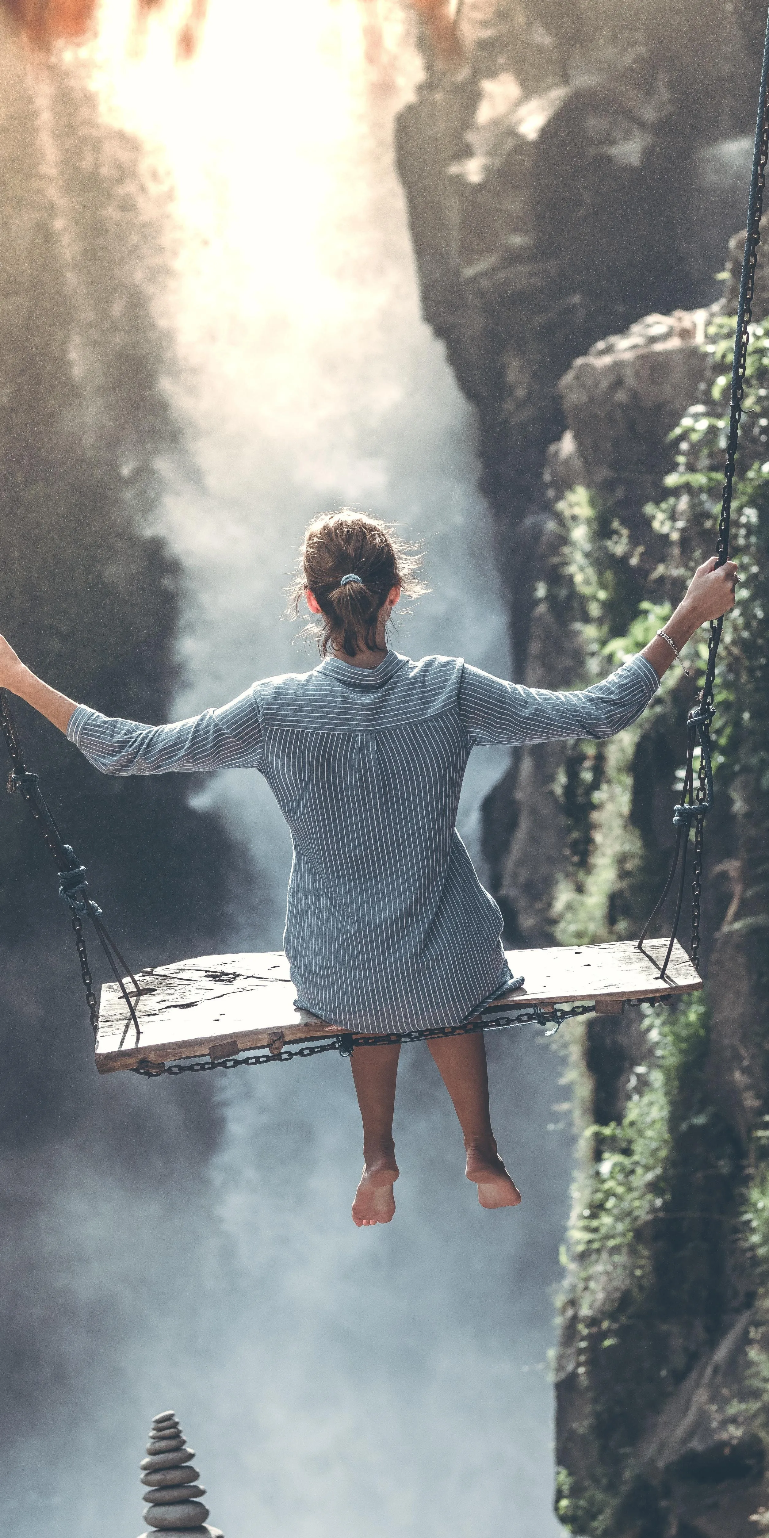 Girl Sitting on Wooden Swing Overlooking Misty Waterfall View