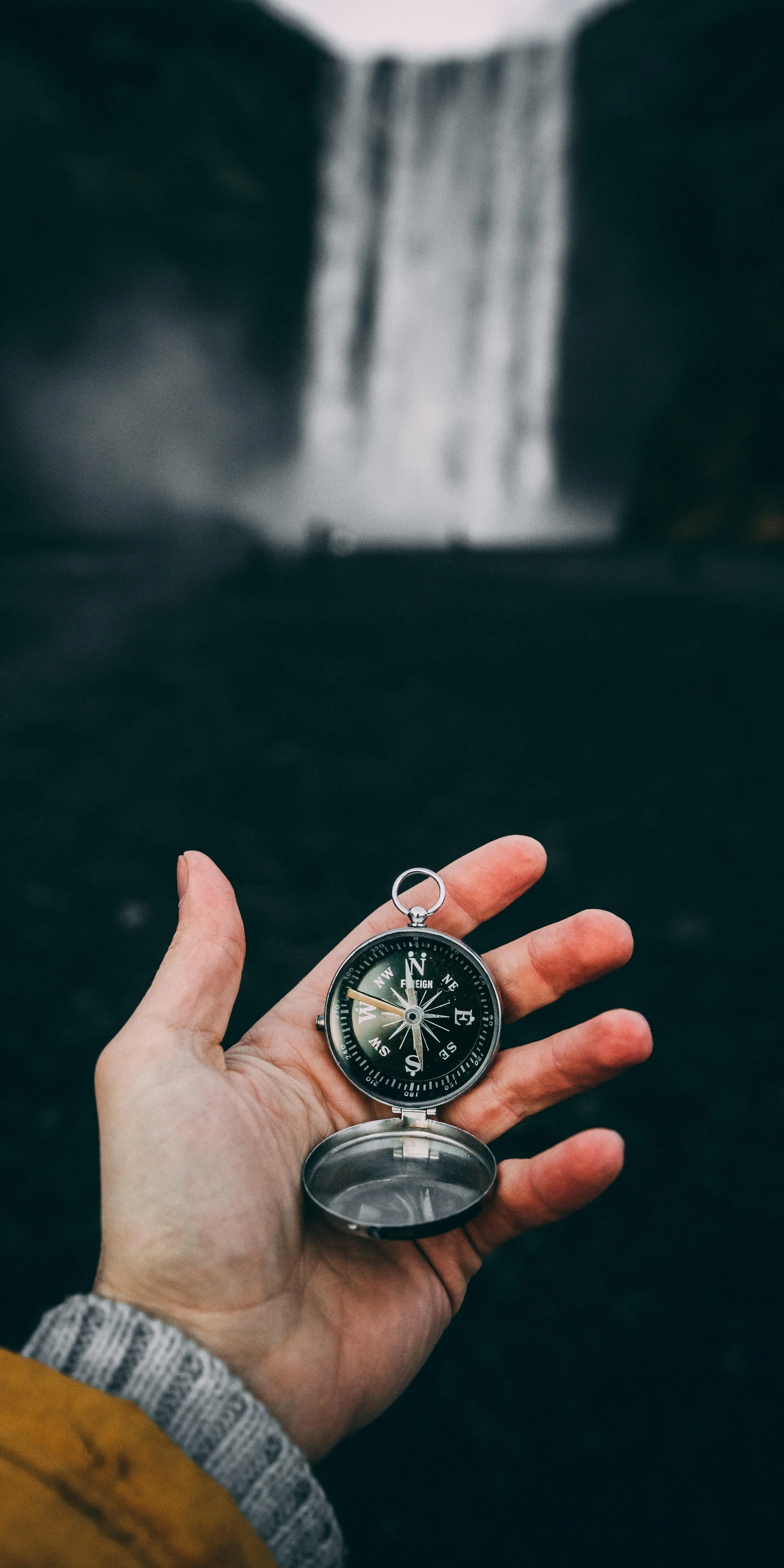 Hand Holding Compass in Front of Waterfall View Wallpaper