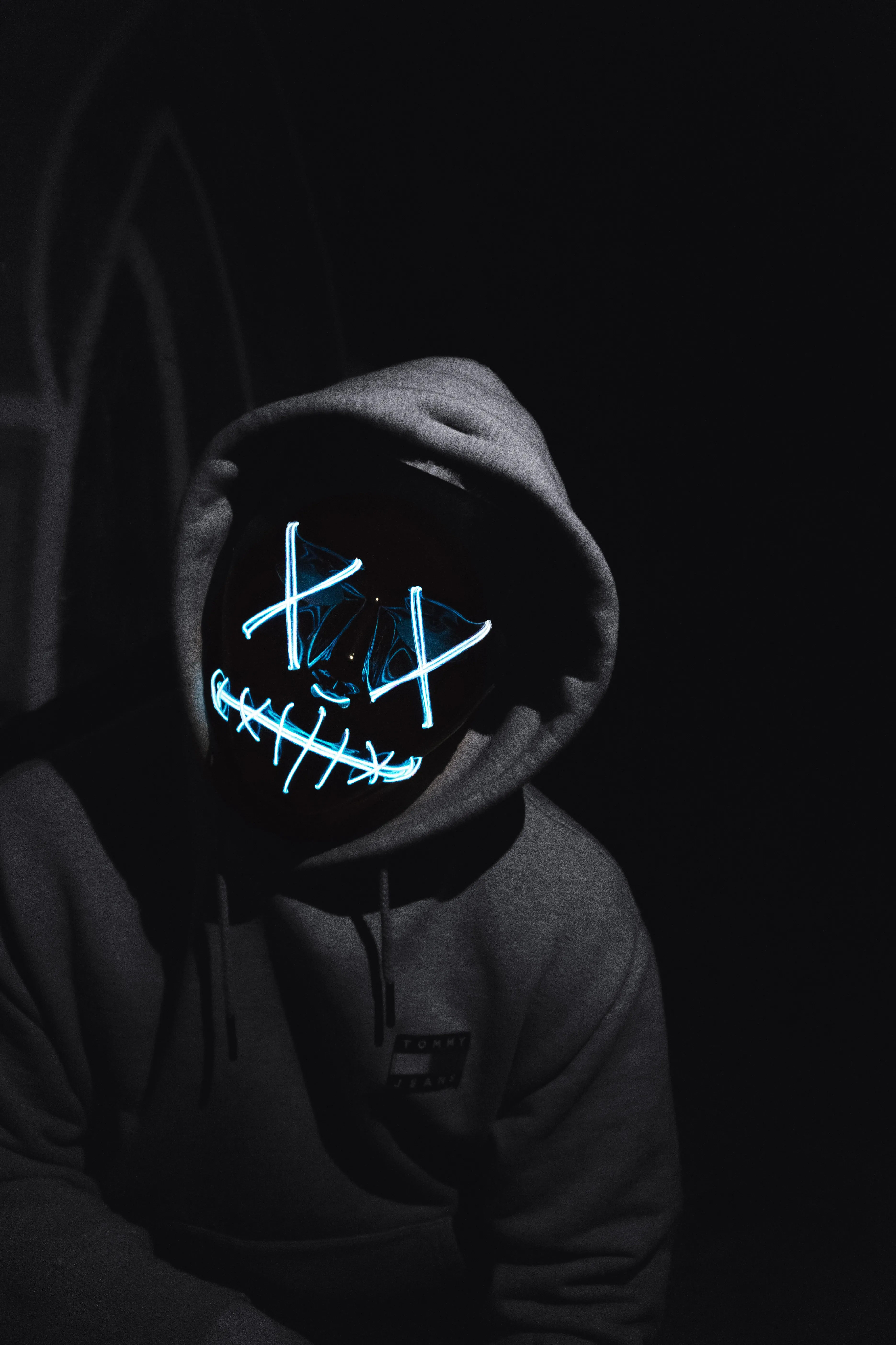 Hooded Figure with Neon Mask in the Dark Wallpaper