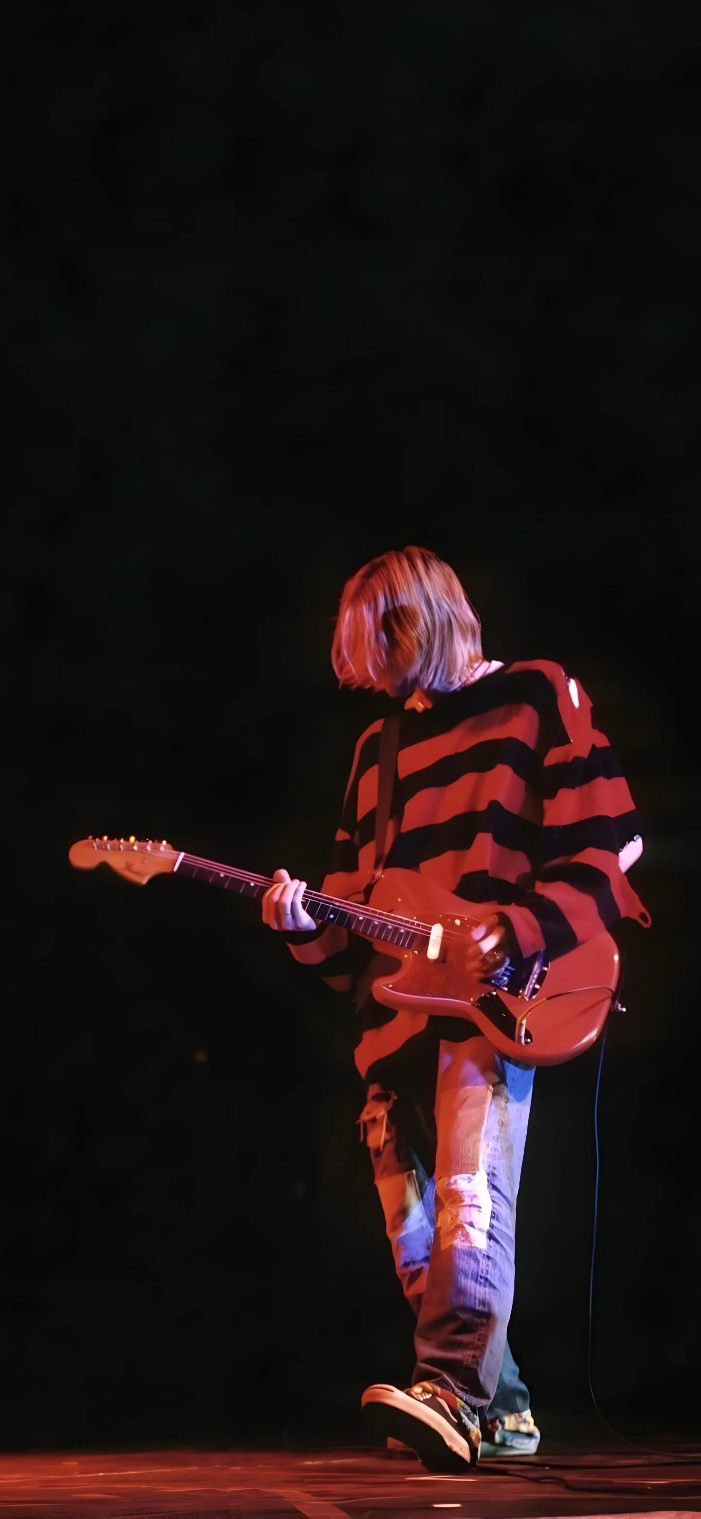 Iconic Guitarist Performing Under Red Stage Lights Image