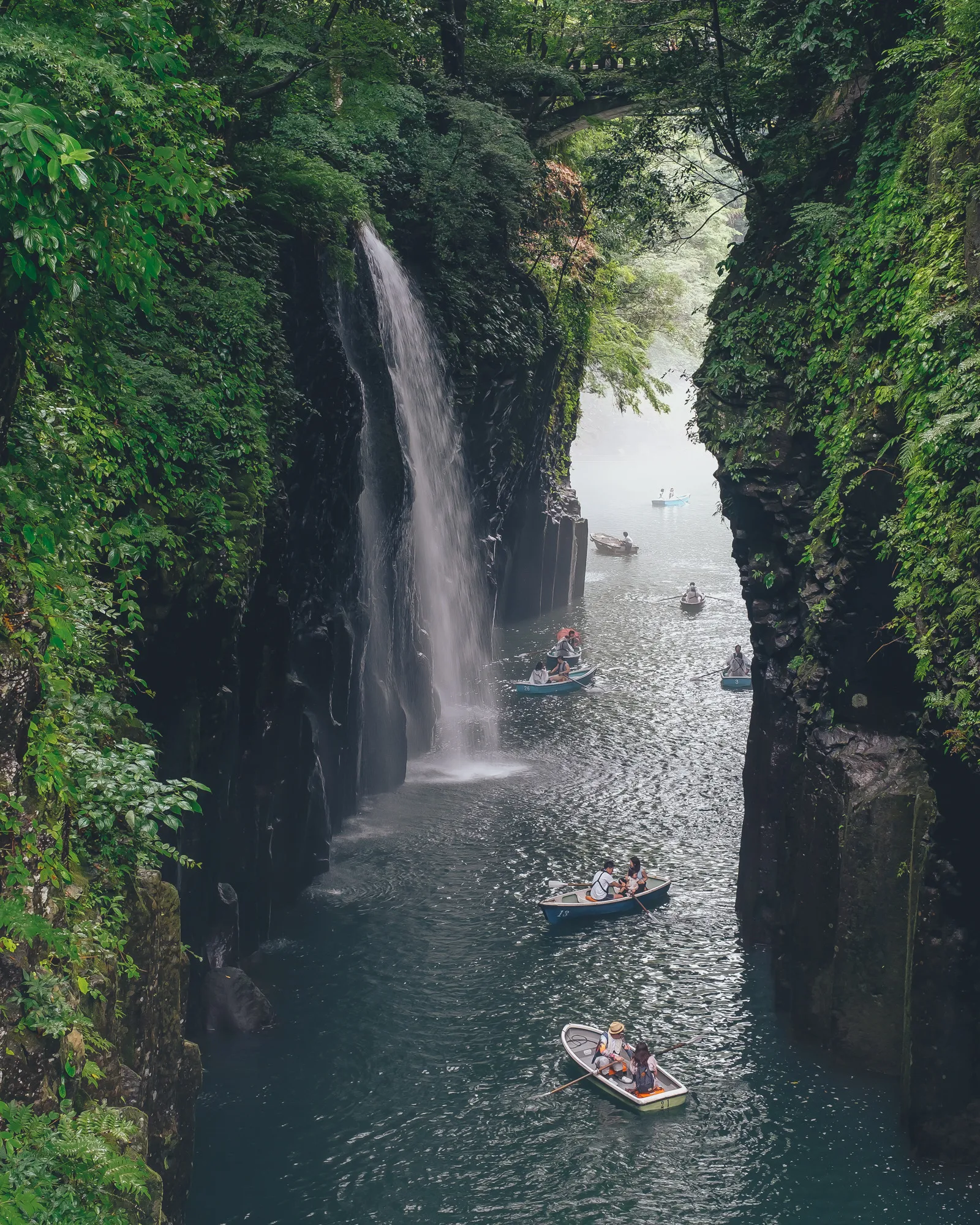 Lush Green River Canyon with Small Boats Passing Through