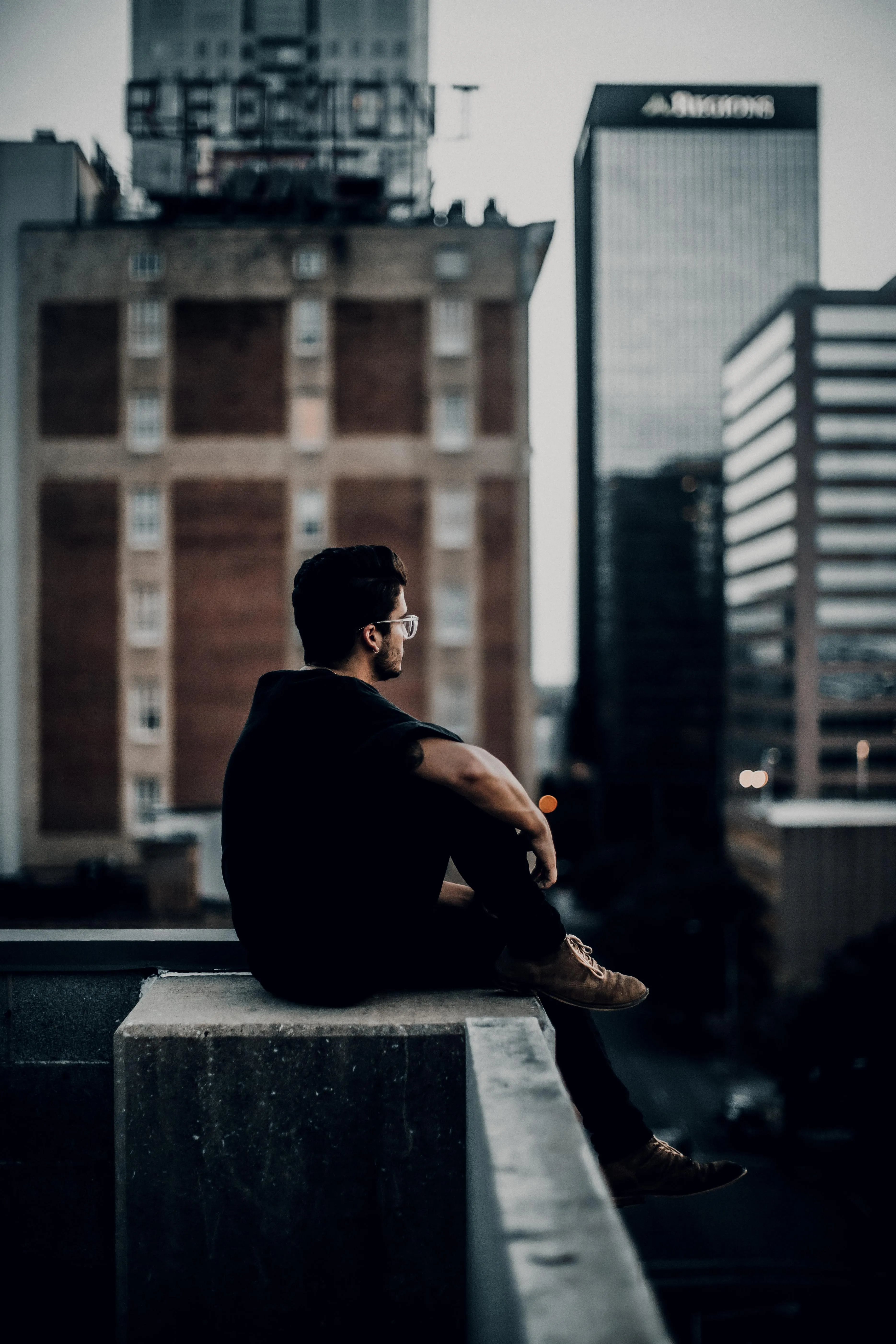 Man Sitting on Rooftop Looking Over City Buildings Image