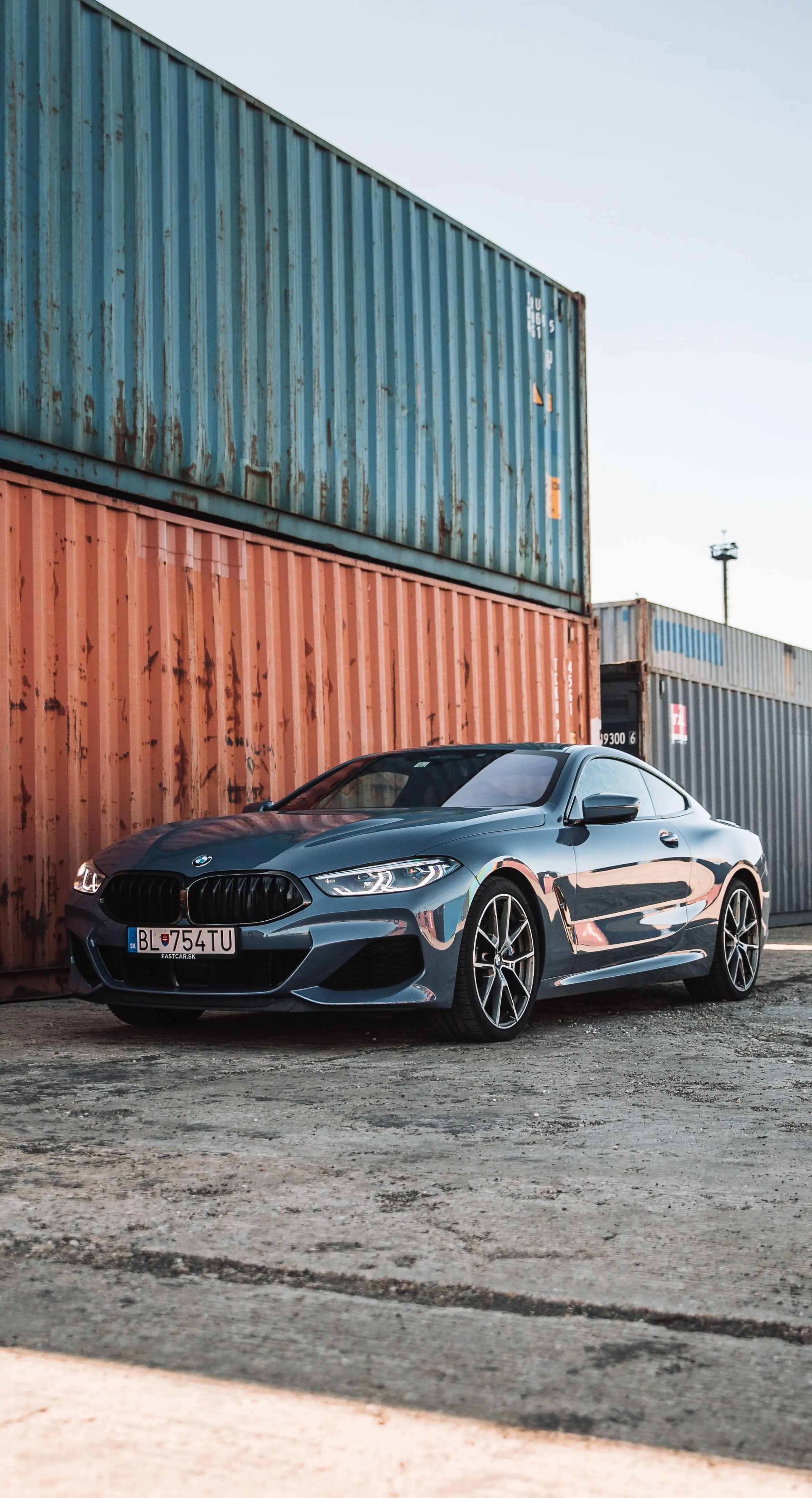Modern Car Parked Near Shipping Containers in Industrial Zone