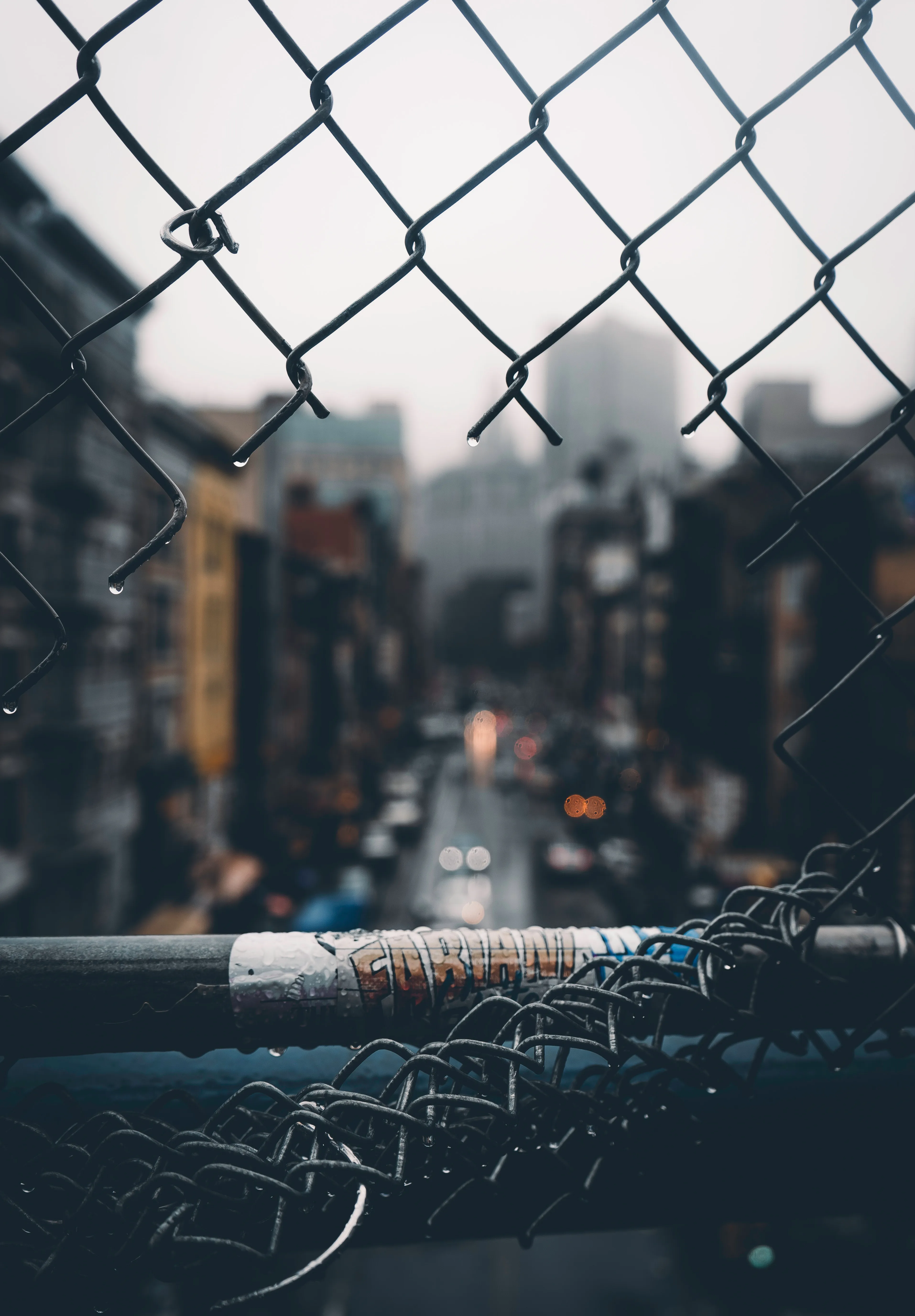 Rain Droplets on Fence with Blurred City Lights Wallpaper