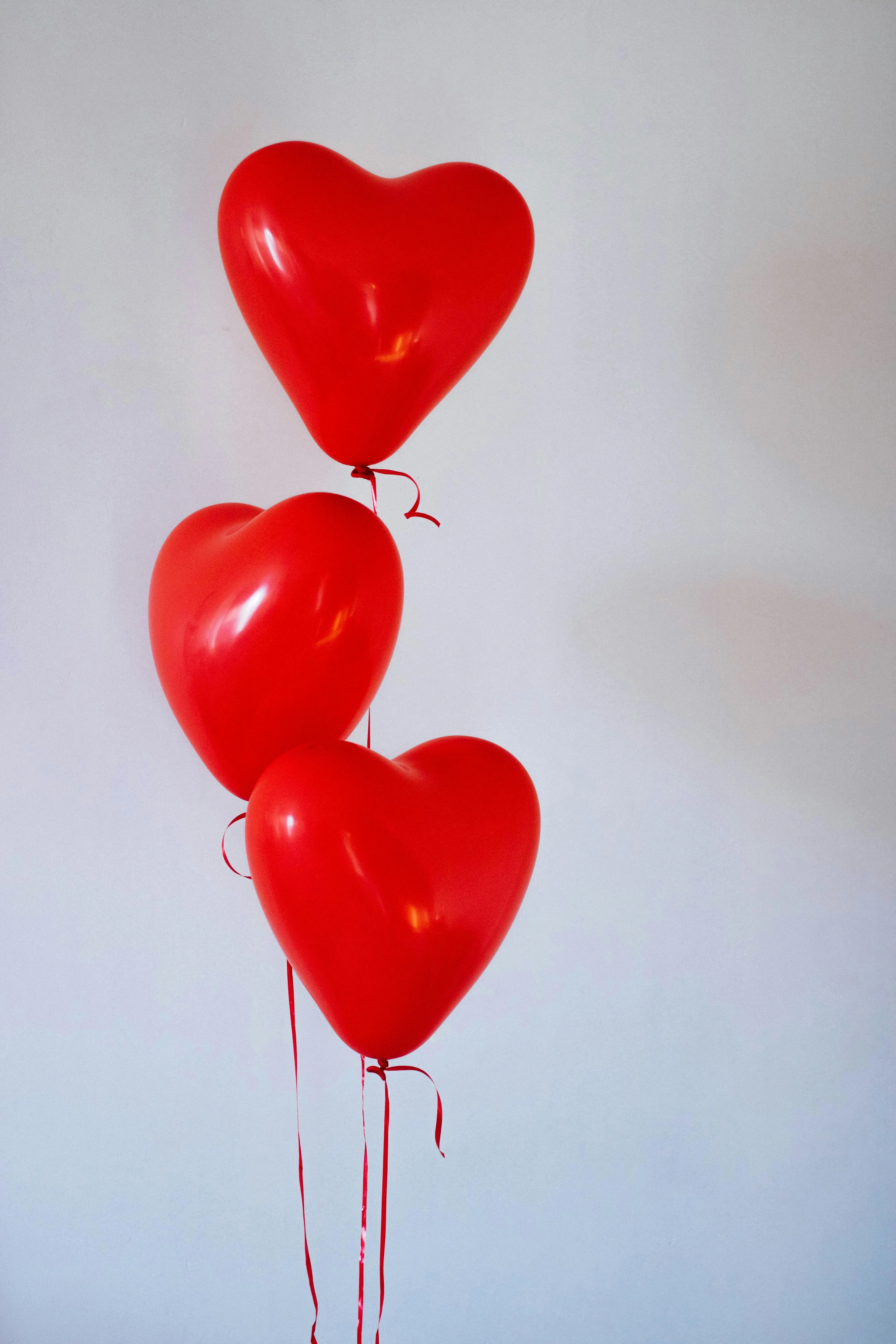 Red Heart Balloons Floating Against White Wall Image