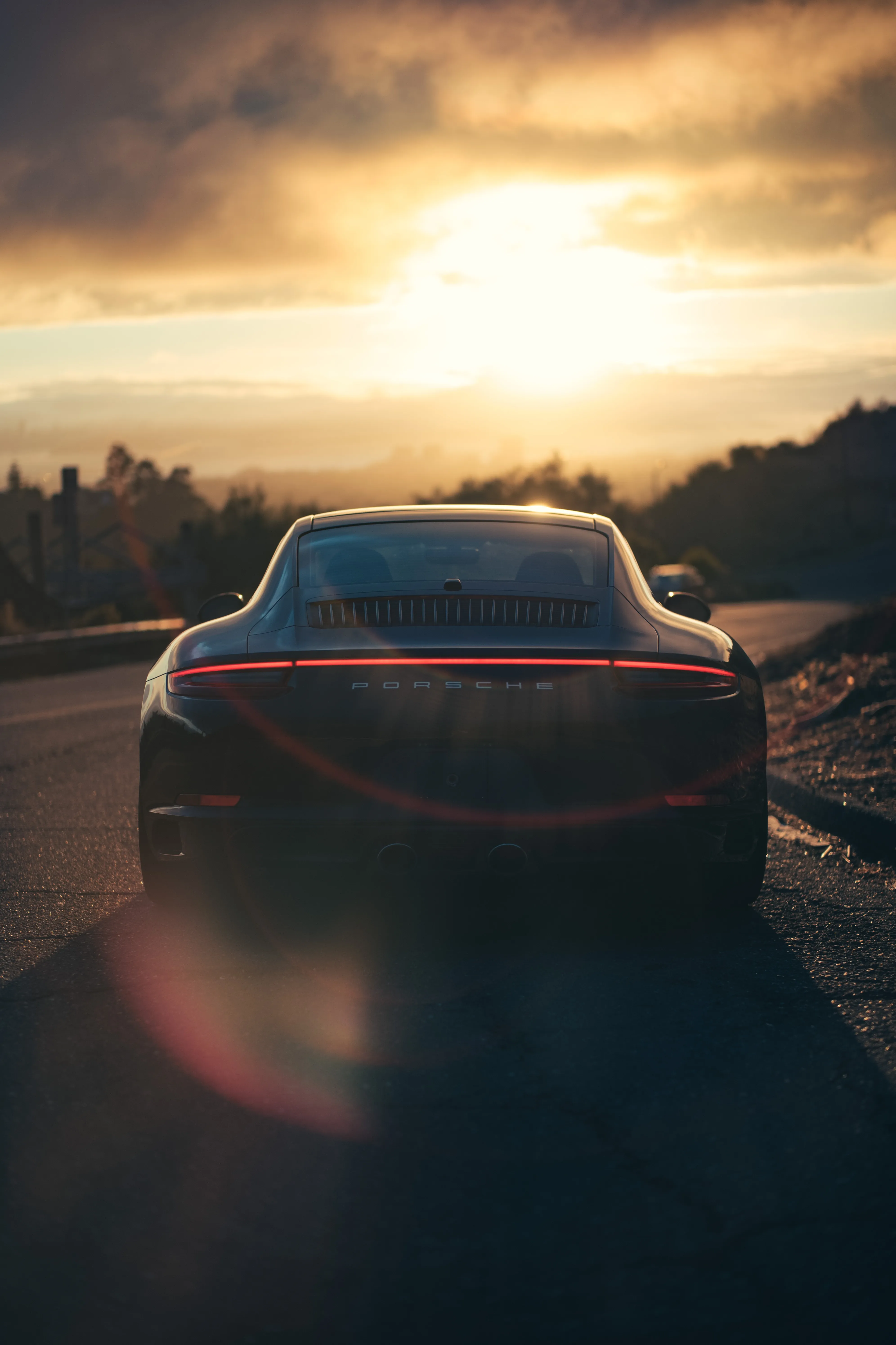 Red Sports Car Driving Into Golden Sunset Glow Wallpaper