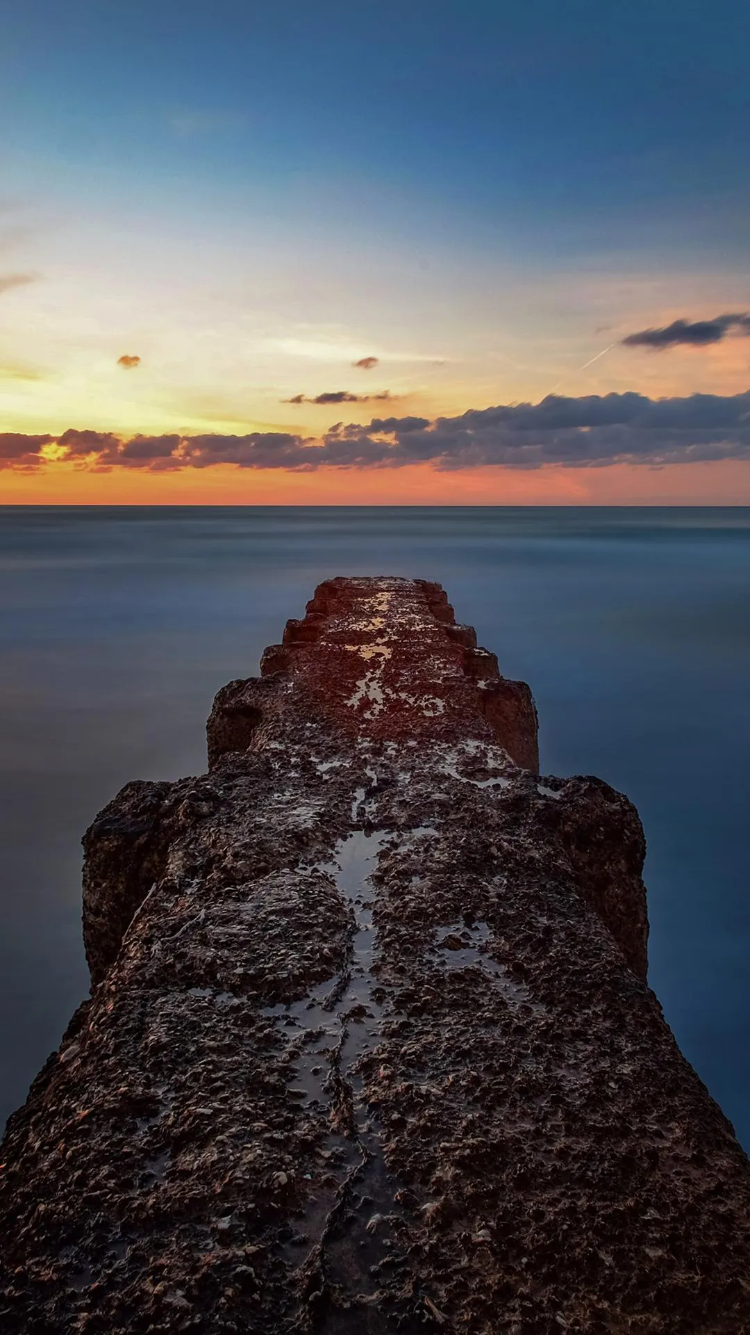 Rocky Pier Leading into Ocean During Sunset Hour Wallpaper