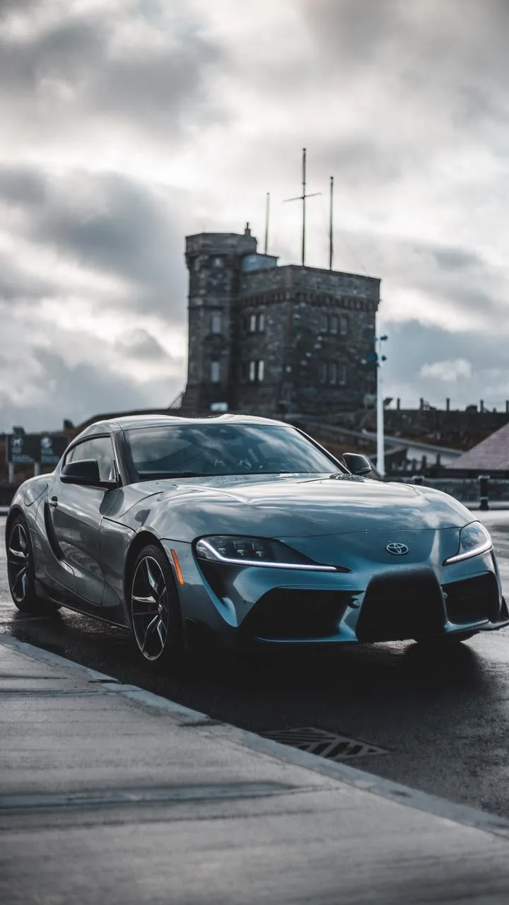 Sports Cars Parked Under Cloudy Urban Sky Scene Wallpaper