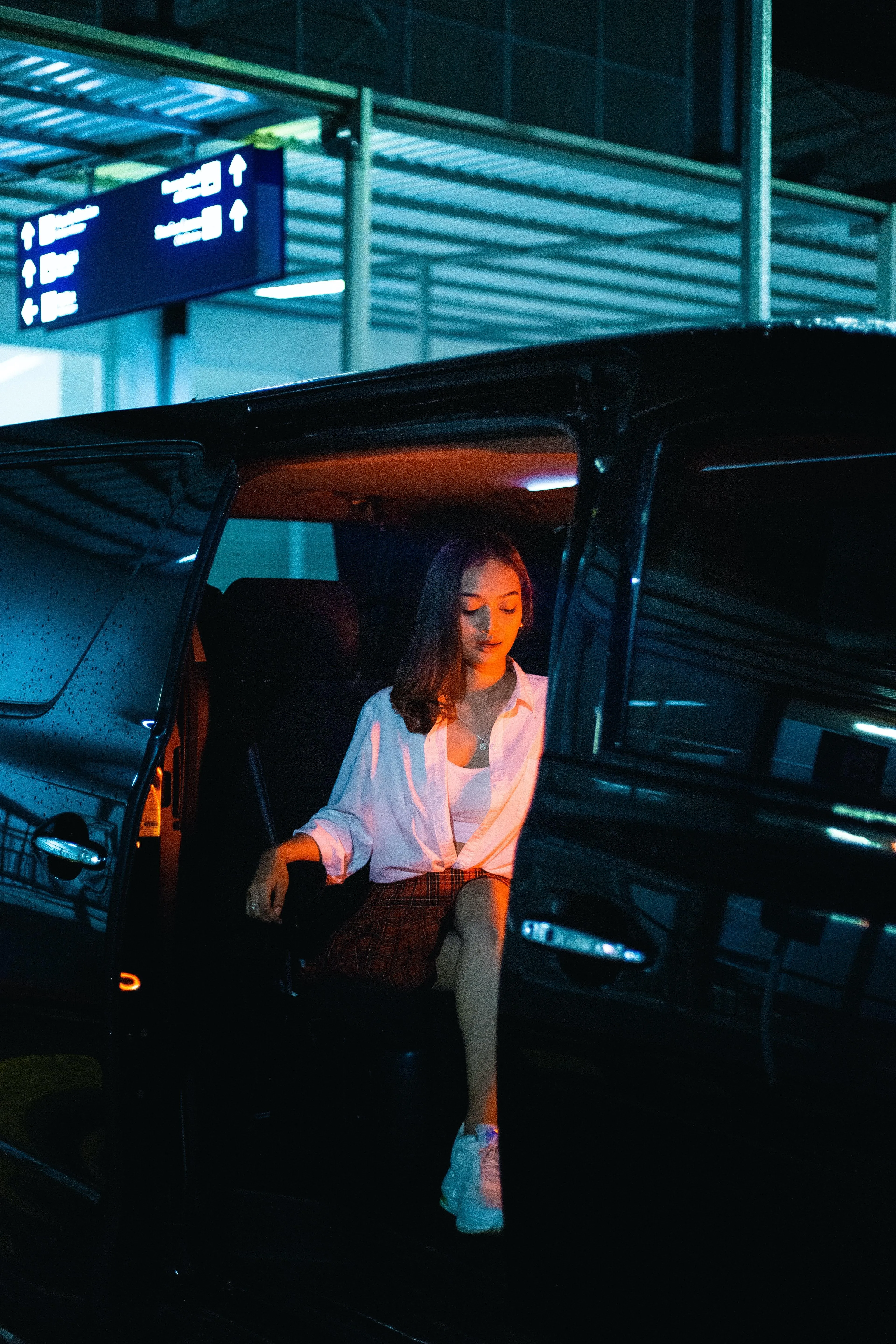Stylish Girl Sitting by Car in Dimly Lit Urban Garage Image