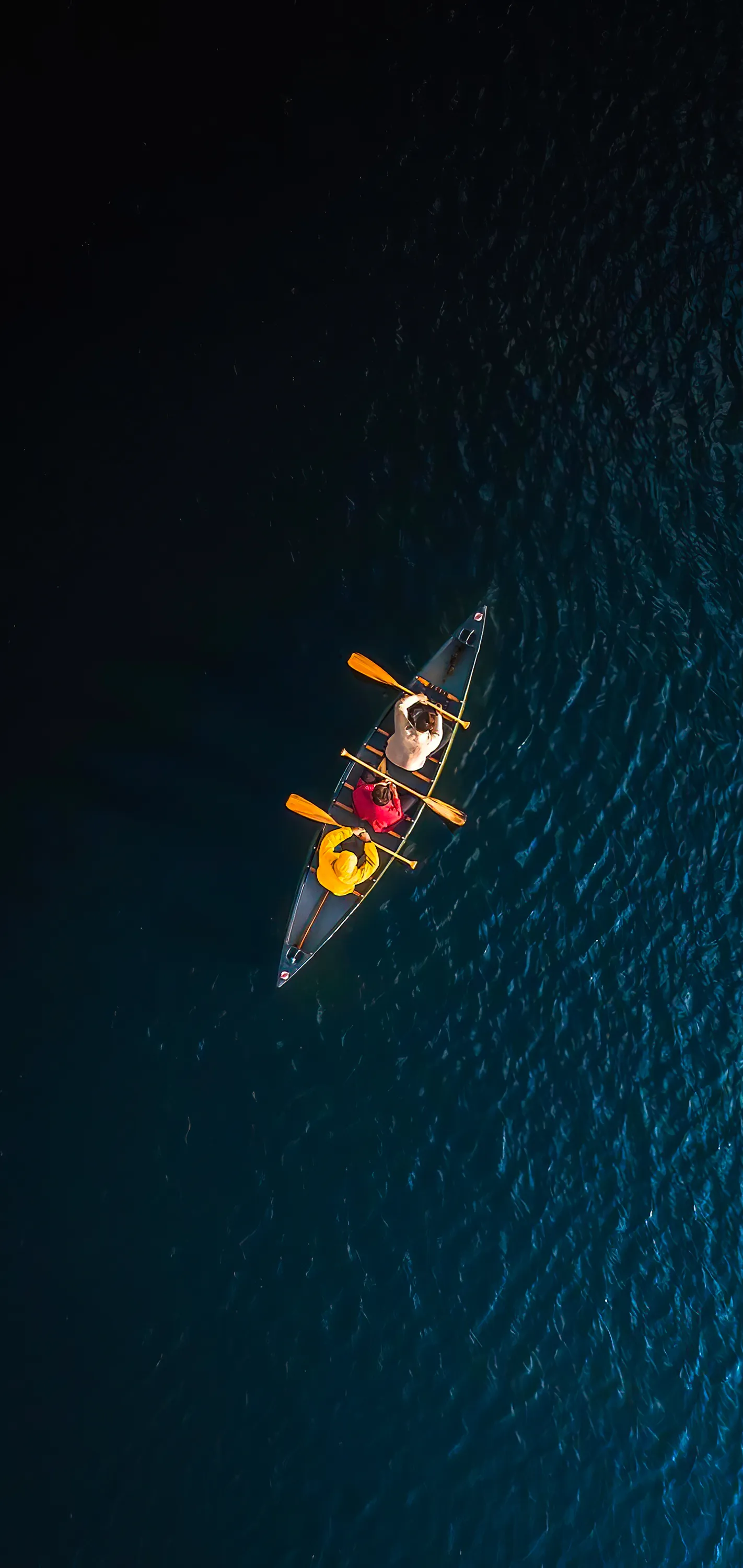 Three People Canoeing Across Deep Blue Water at Sunrise
