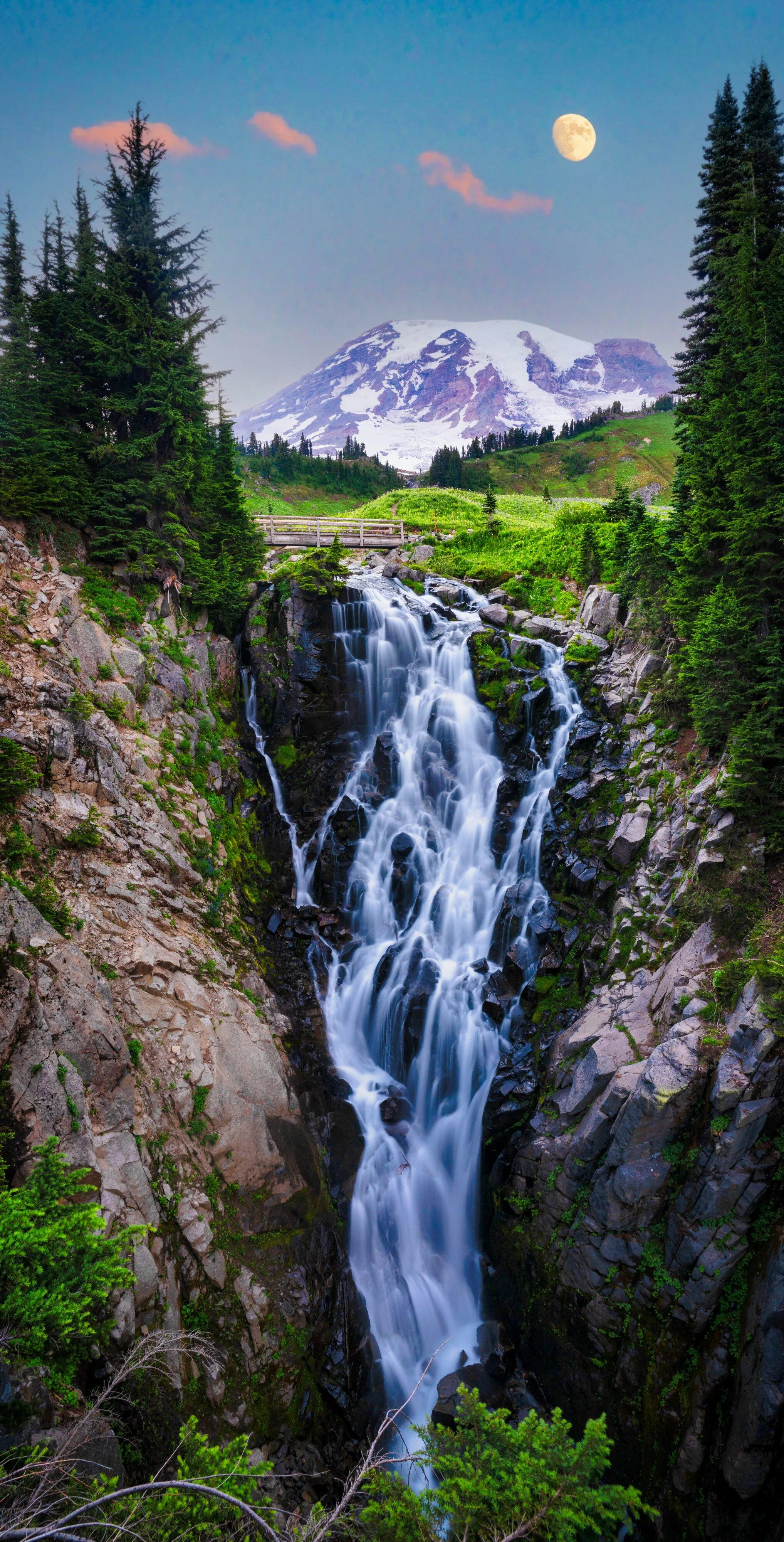 Waterfall Flowing Through Forest with Distant Snowy Peaks